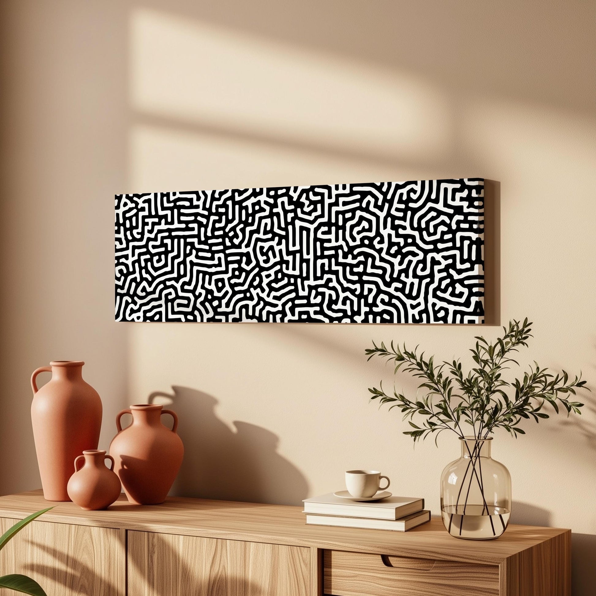 a wooden cabinet with three orange vases, a white coffee cup, and a stack of books on top. Above the cabinet, there is a large abstract painting with a black and white pattern.