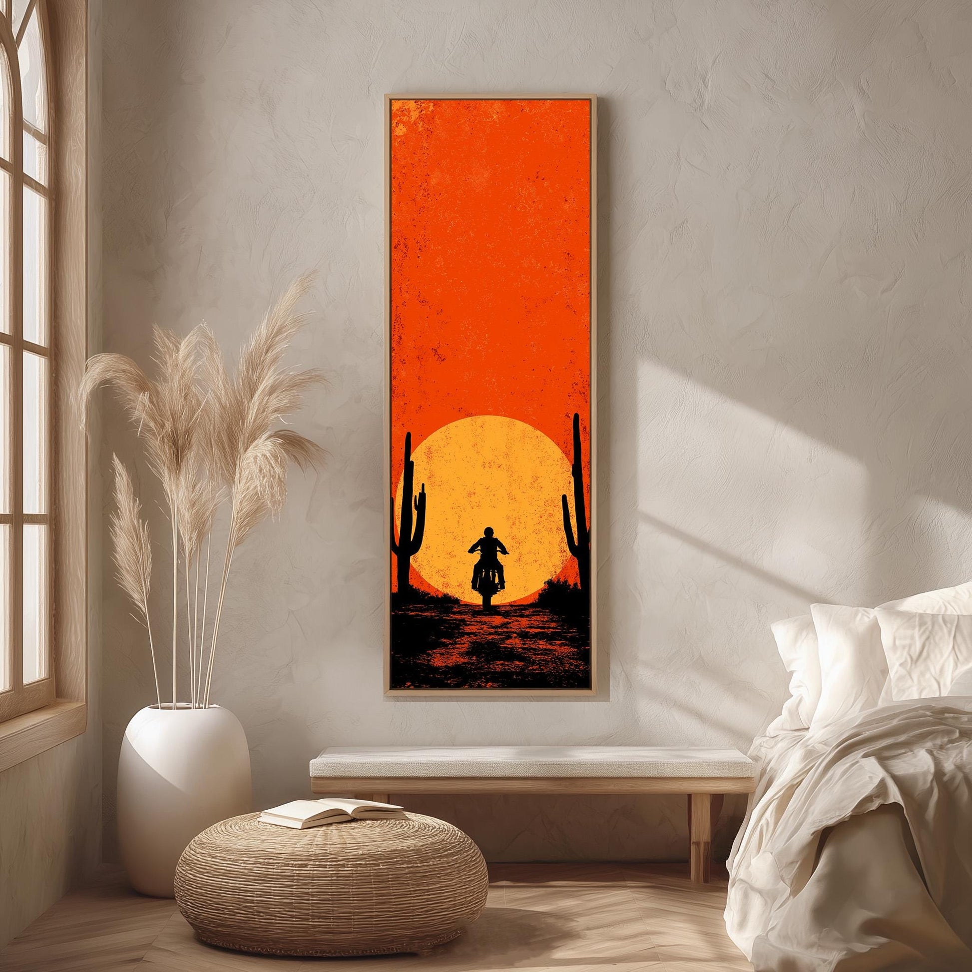 a large, vibrant orange and black poster of a desert scene with a silhouette of a person riding a motorcycle against the backdrop of a sunset. The poster is hanging on a wall in a room with a bed, a potted plant, and a woven ottoman.