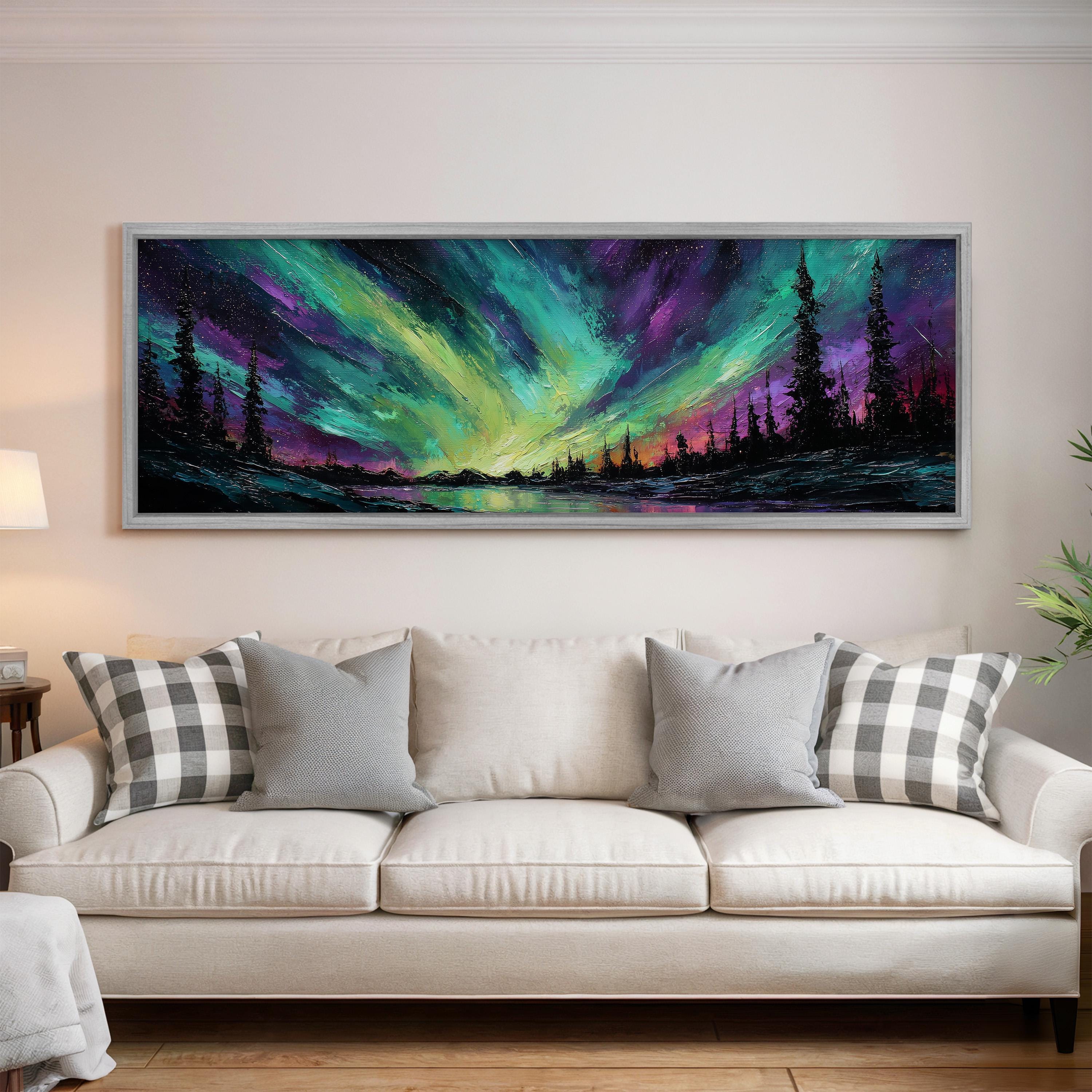 a large, colorful painting of a night sky with a stunning display of the Aurora Borealis, or Northern Lights, over a landscape with trees and a lake. The painting is hung on a wall above a white couch, creating a cozy and artistic atmosphere in the living room.