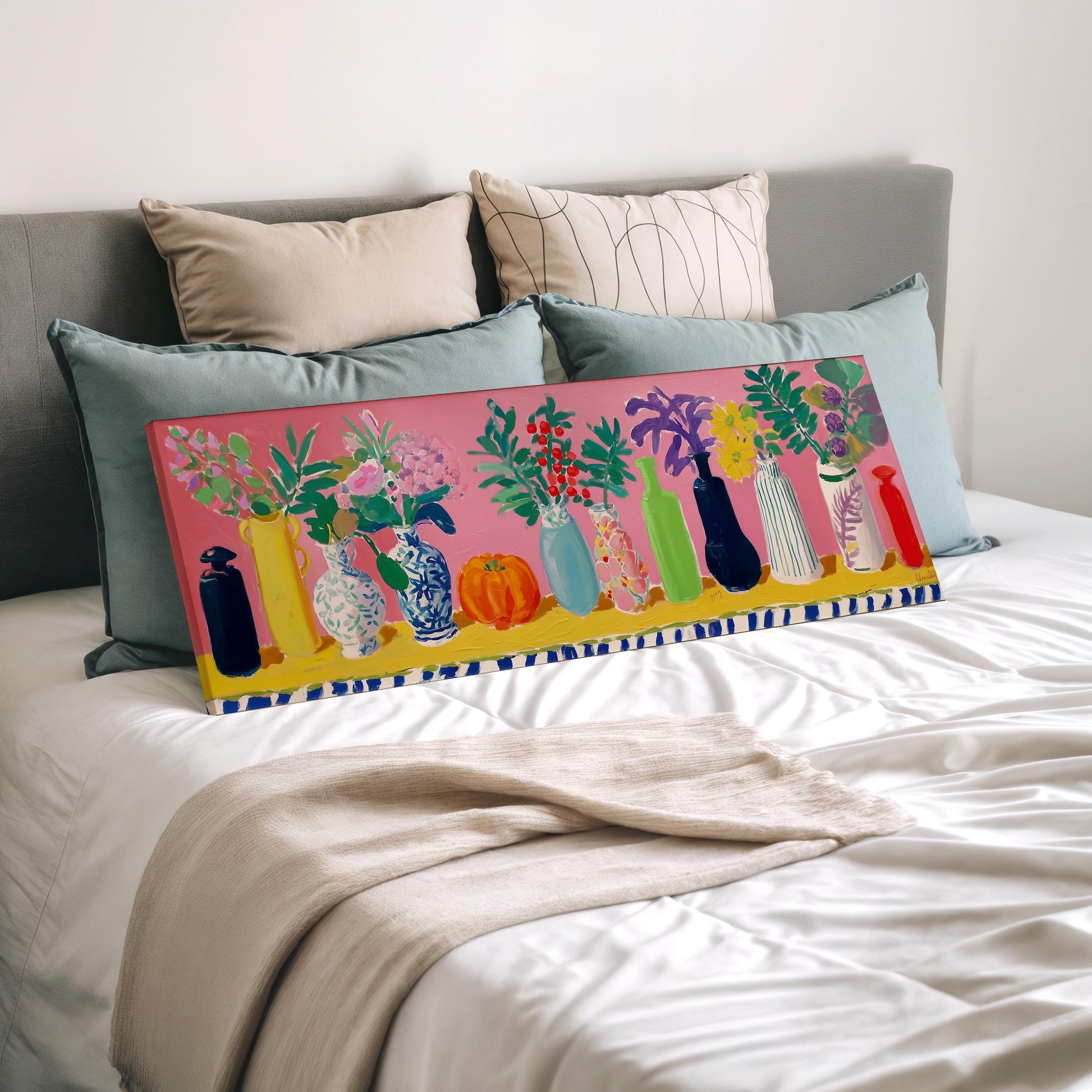 a bed with a colorful painting of vases and flowers on it, along with a beige blanket and pillows.