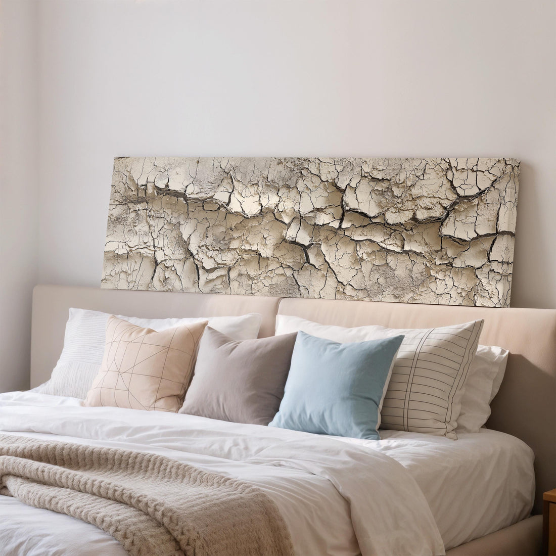 a bedroom with a bed covered in white sheets and pillows, and a large, textured, cracked wall art piece above the bed.