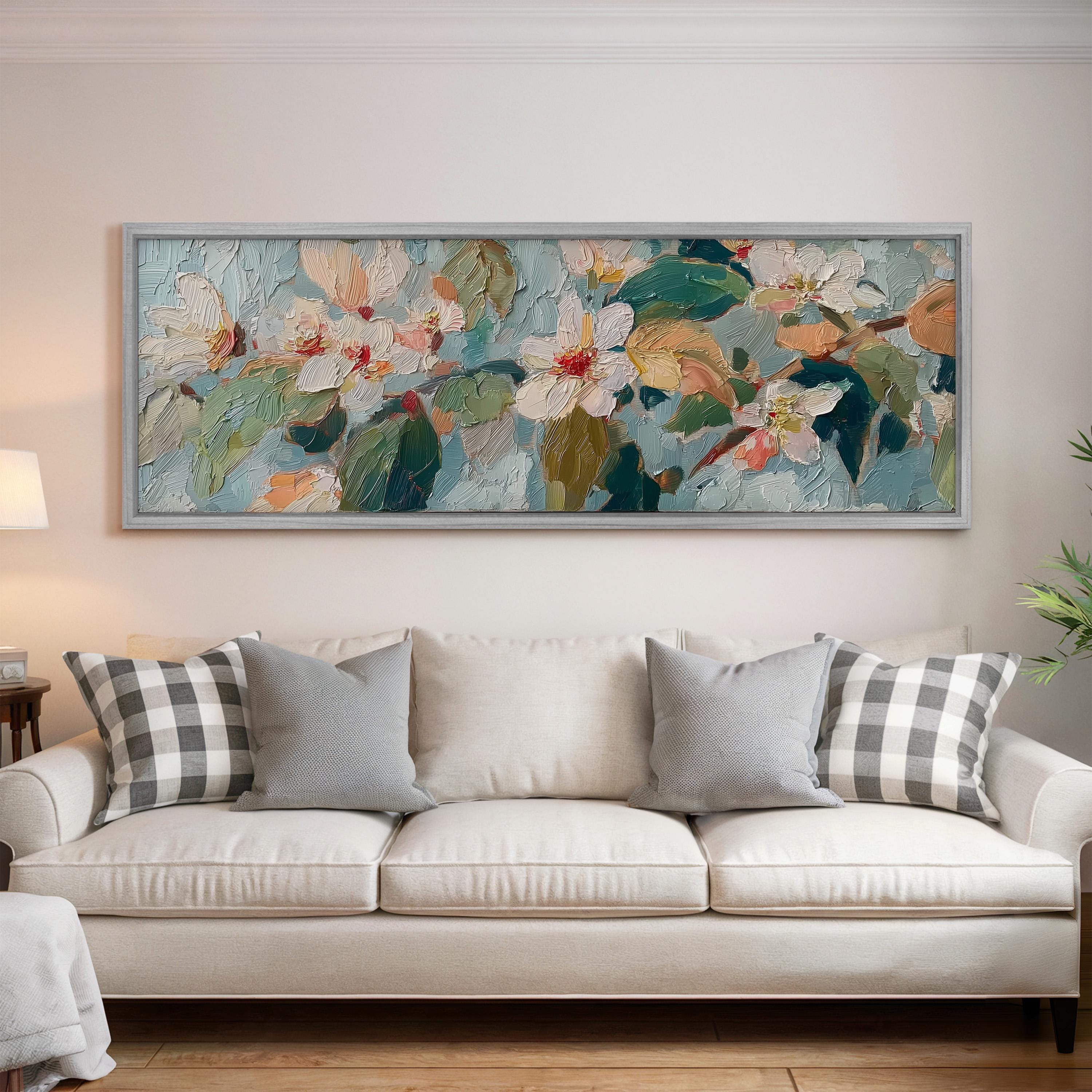a large, colorful painting of flowers hanging on a wall above a white couch with gray and white plaid throw pillows.