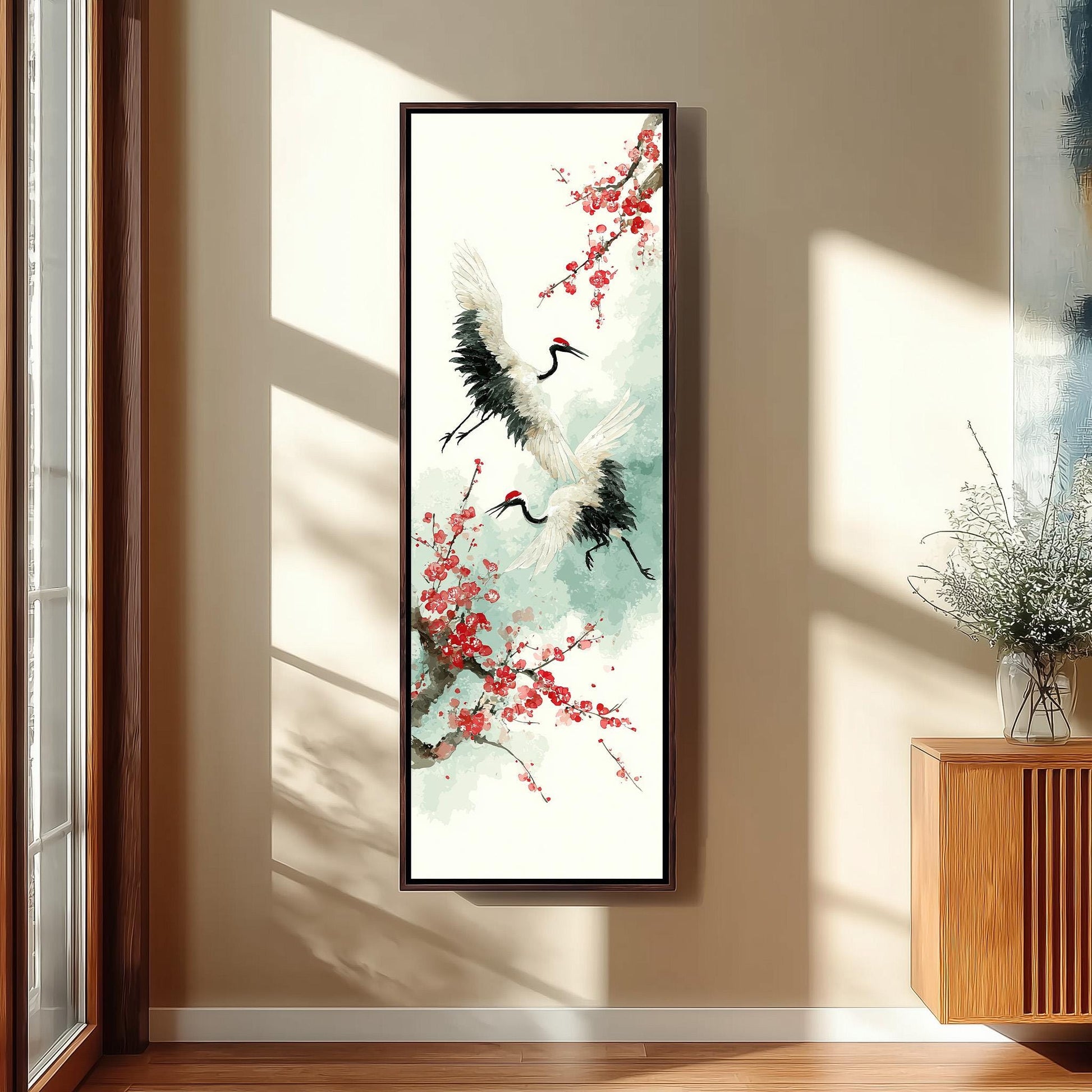 a large framed painting of two white birds with black beaks and legs, surrounded by red flowers, hanging on a wall in a room with a wooden cabinet and a vase of flowers.