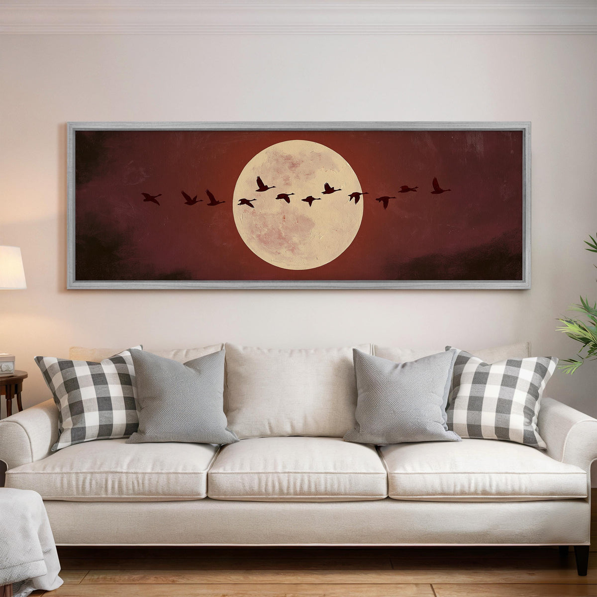 Geese crossing a pale moon on maroon panoramic canvas print above a white sofa in a bright living room