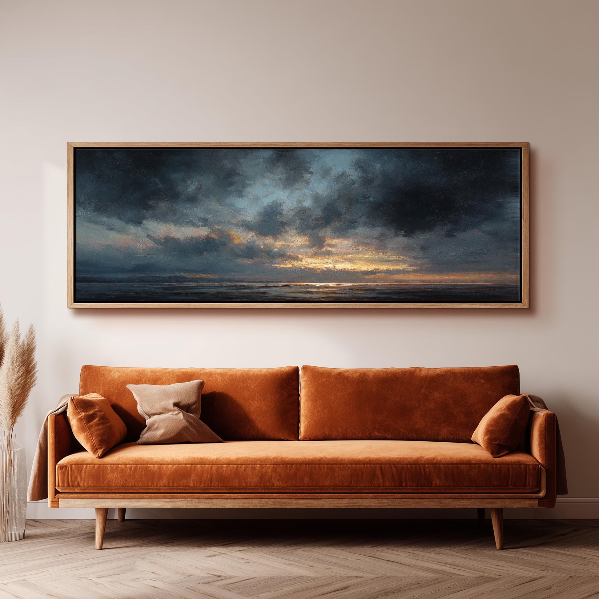 a large, framed painting of a serene landscape depicting a sunset over the ocean, hanging on a wall above a brown sofa with orange cushions.