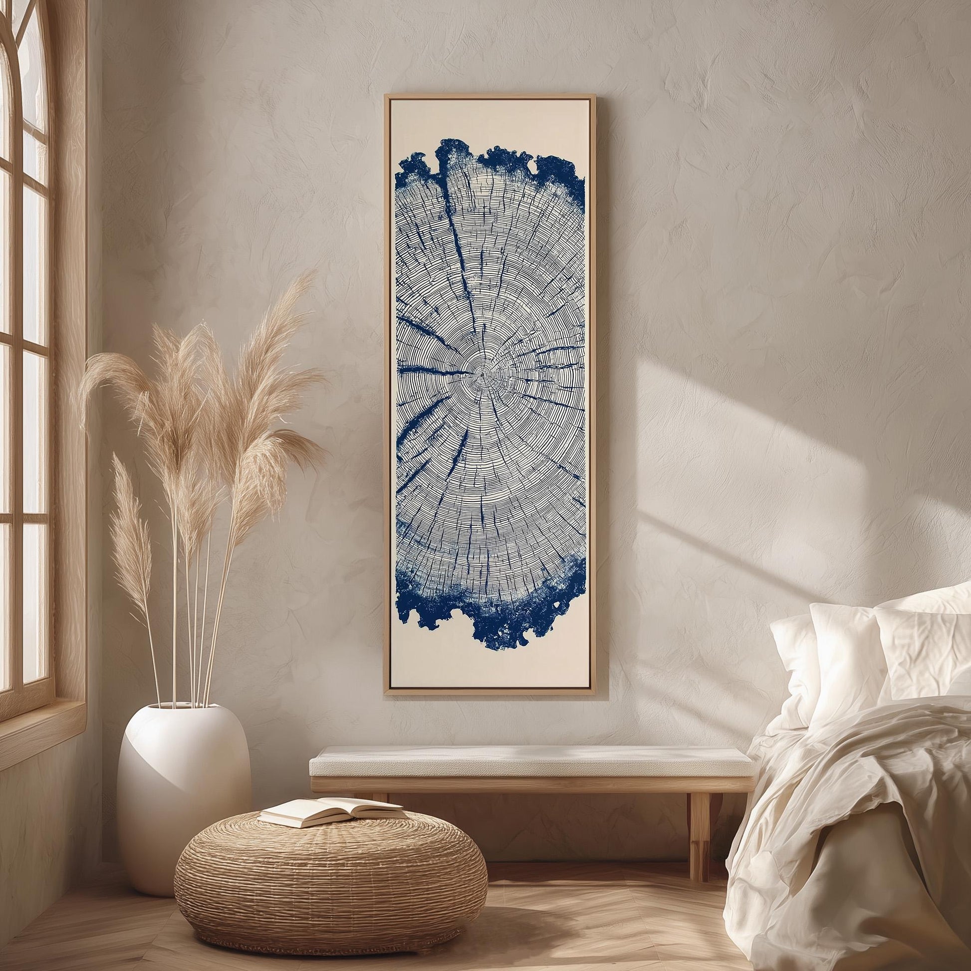 a serene bedroom scene with a large tree stump print hanging on the wall, a white bed with white pillows, a white wicker ottoman, and a window with white curtains.