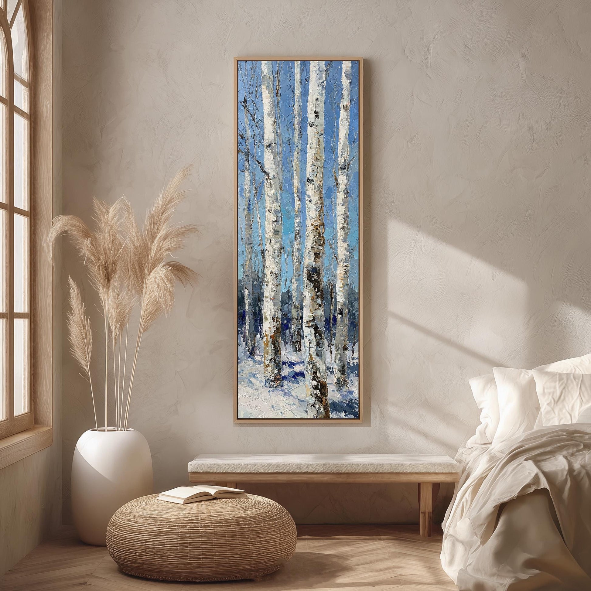 a serene indoor setting with a large painting of a snowy forest hanging on the wall, a white bed with a white pillow and blanket, a white vase with tall potted plants, and a woven ottoman in the foreground.