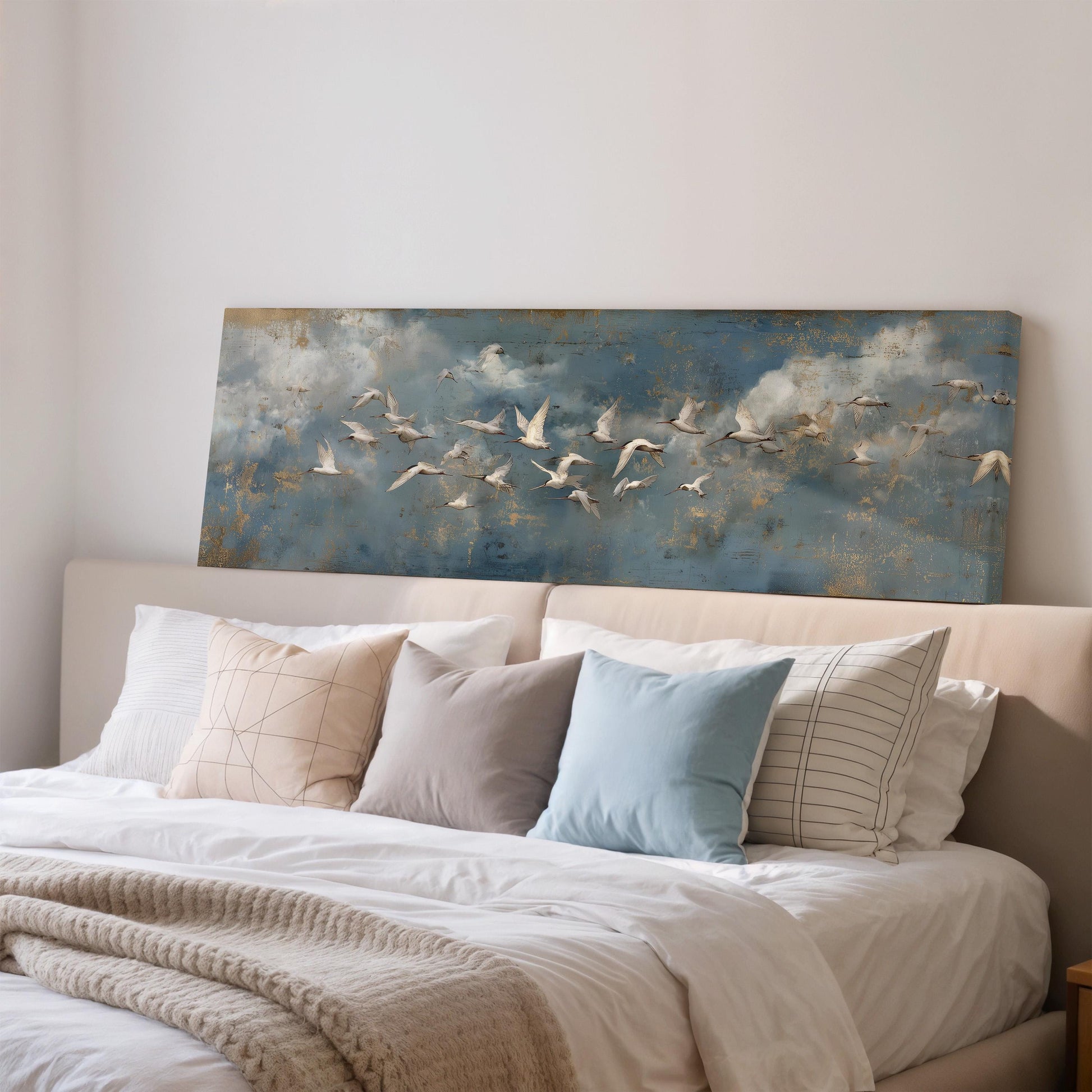 a bedroom with a large bed covered in white sheets and pillows. Above the bed, there is a painting of a flock of white birds flying across a blue sky with clouds.