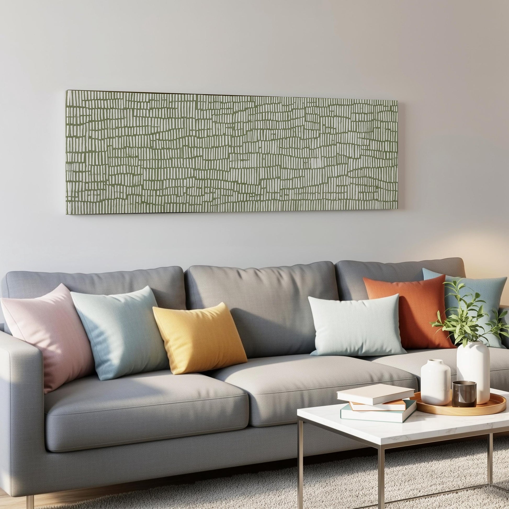 a modern living room with a gray sofa adorned with colorful throw pillows. Above the sofa, there is a large abstract painting on the wall. In front of the sofa, there is a white coffee table with a stack of books and a small plant.