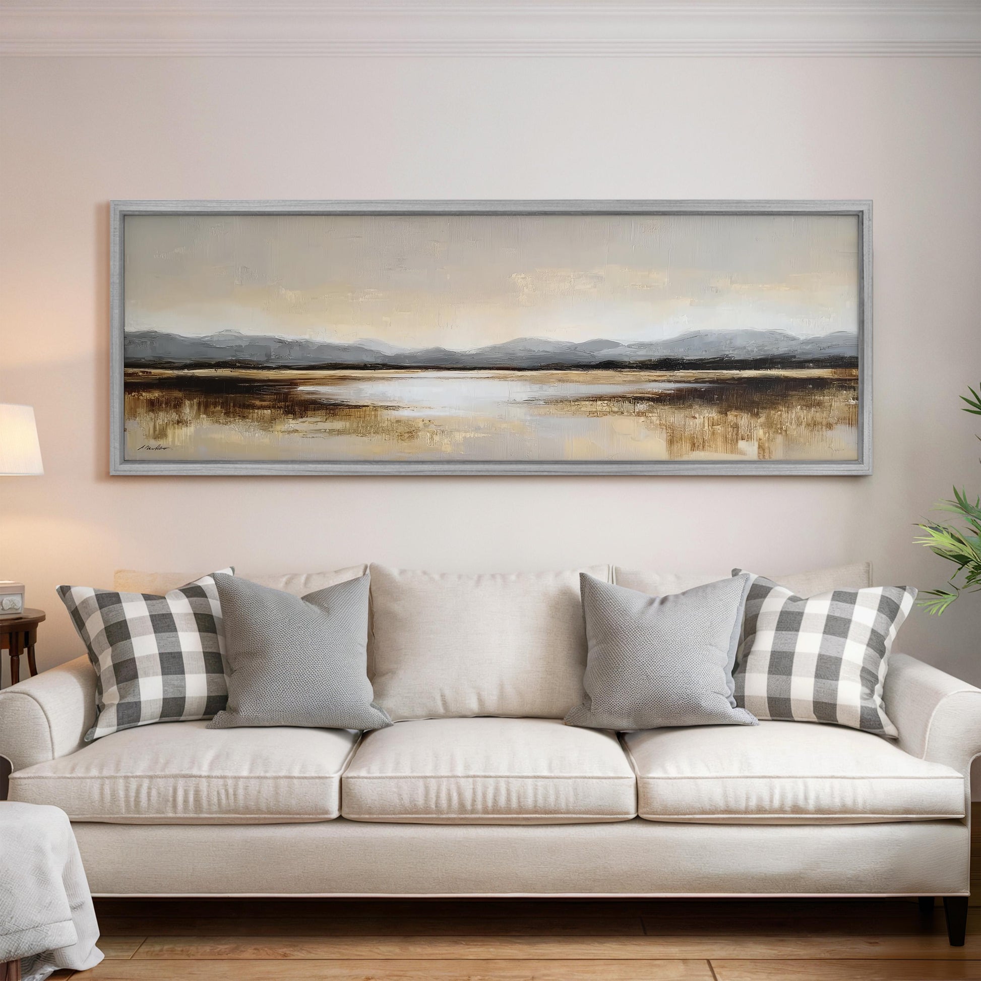 a large, framed landscape painting hanging on a wall above a white sofa with gray and white patterned throw pillows.