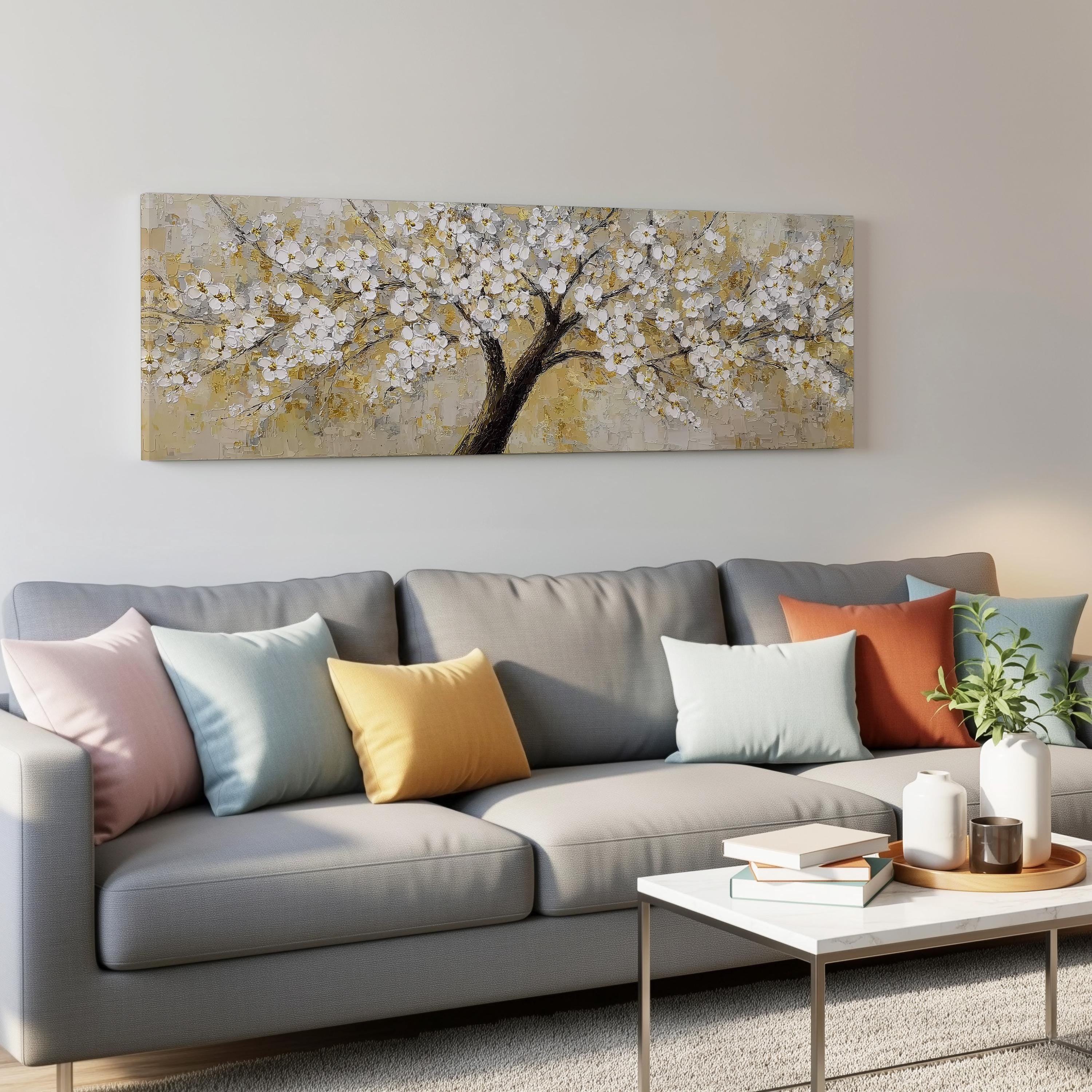 a gray couch with colorful throw pillows, a coffee table, and a large painting of a tree with white flowers hanging on the wall above the couch.