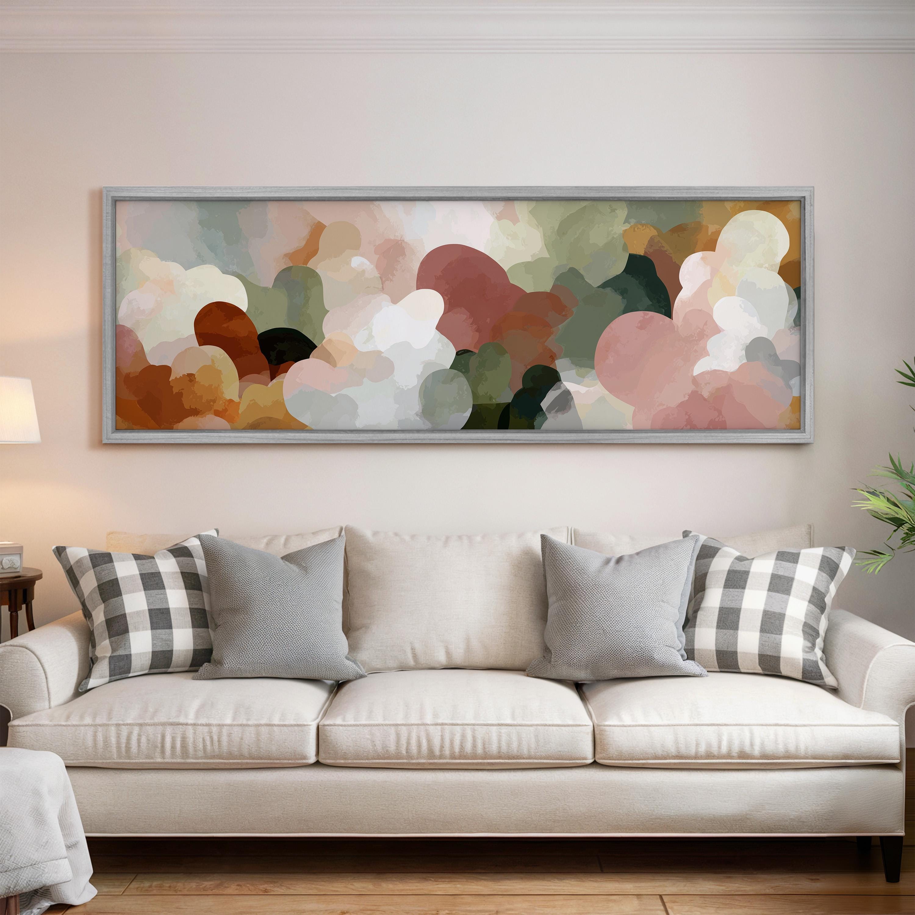 a large abstract painting hanging on a wall above a white sofa with gray and white plaid throw pillows.