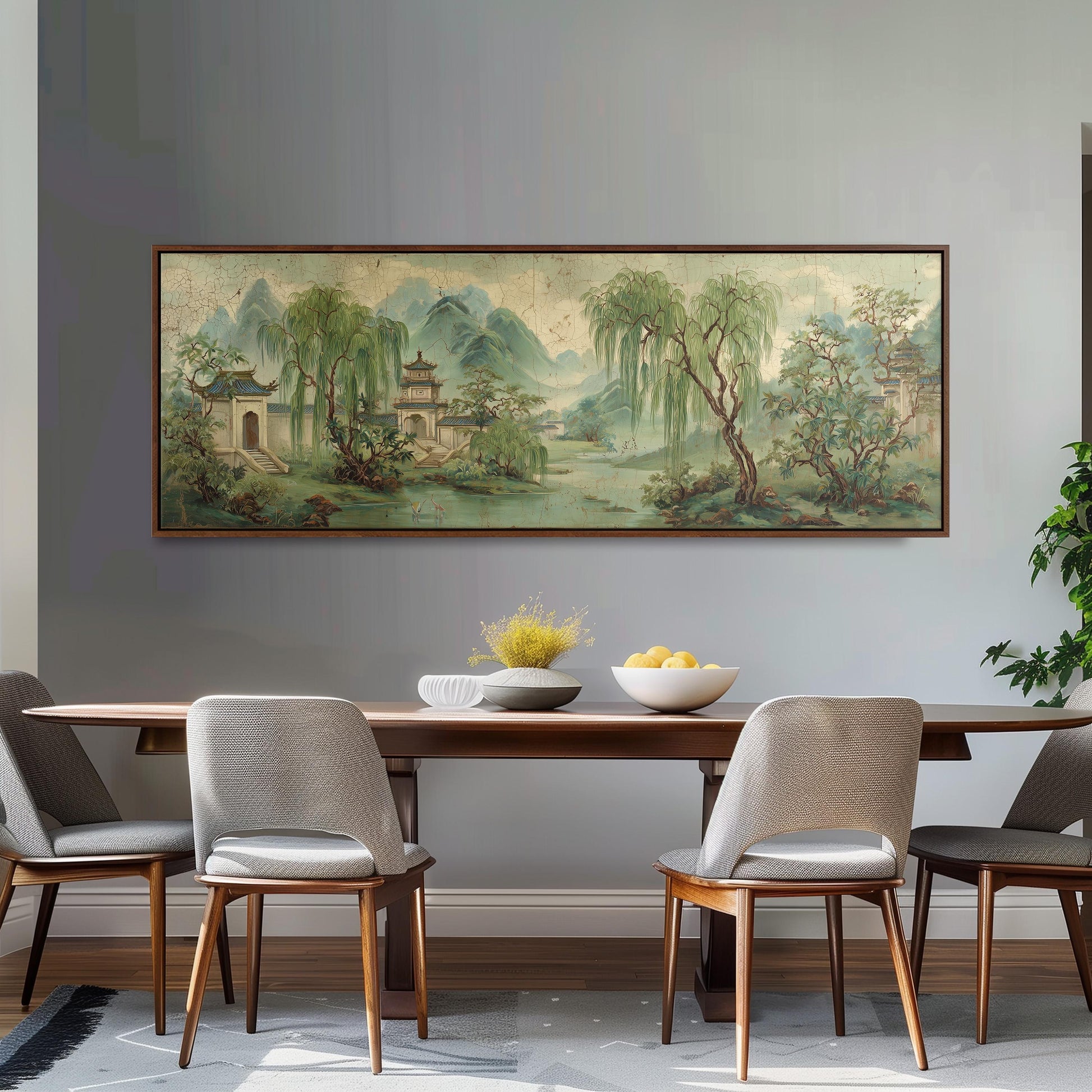 a dining room with a large painting of a serene landscape hanging on the wall above a wooden dining table with four chairs. The painting depicts a tranquil scene with a temple, trees, and a river, creating a peaceful atmosphere.