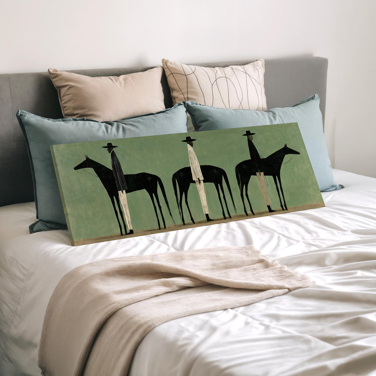 Three stylized cowboys with horses on sage green wide panoramic canvas print laid on a bed to show its size
