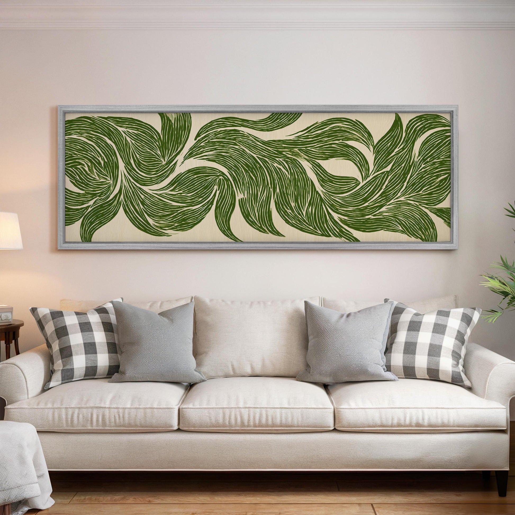a large, framed artwork of green leaf patterns hanging on a wall above a white couch with gray and white plaid throw pillows.