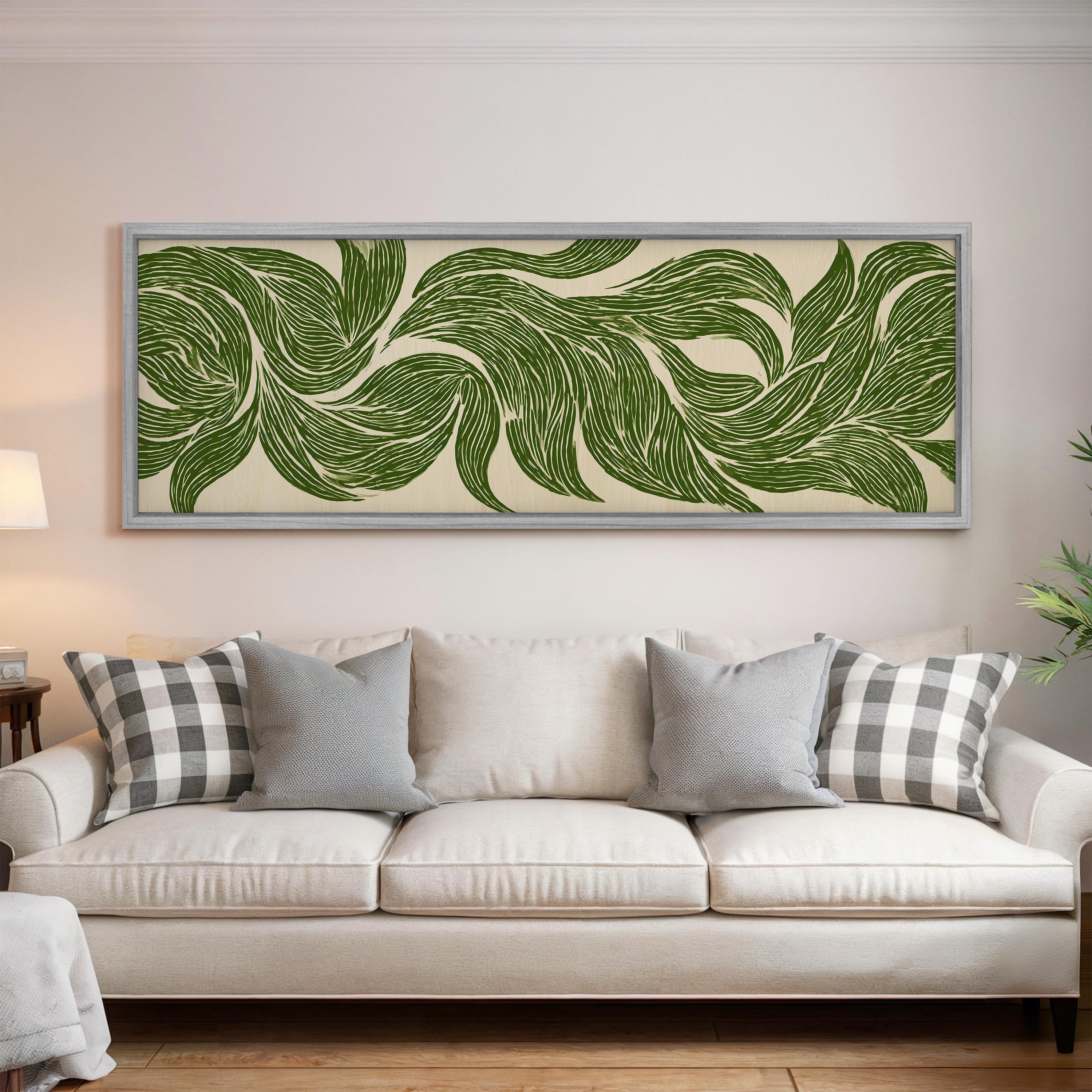 a large, framed artwork of green leaf patterns hanging on a wall above a white couch with gray and white plaid throw pillows.