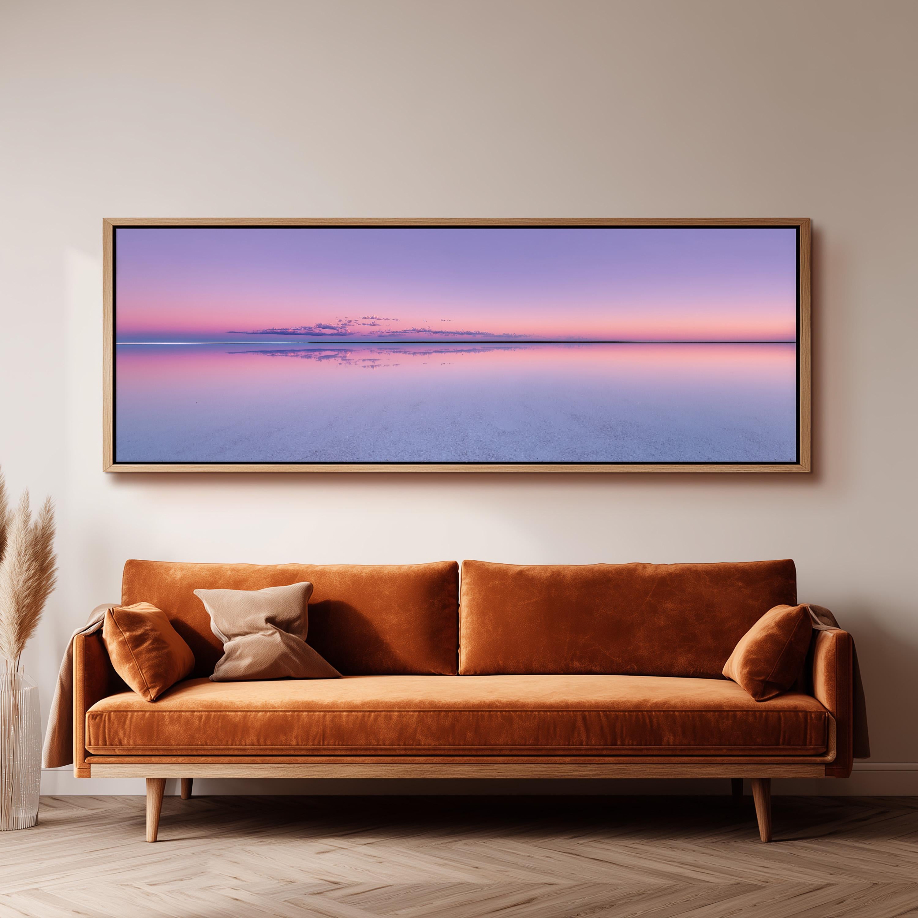 a large, rectangular painting hanging on a wall above a brown sofa with two pillows.