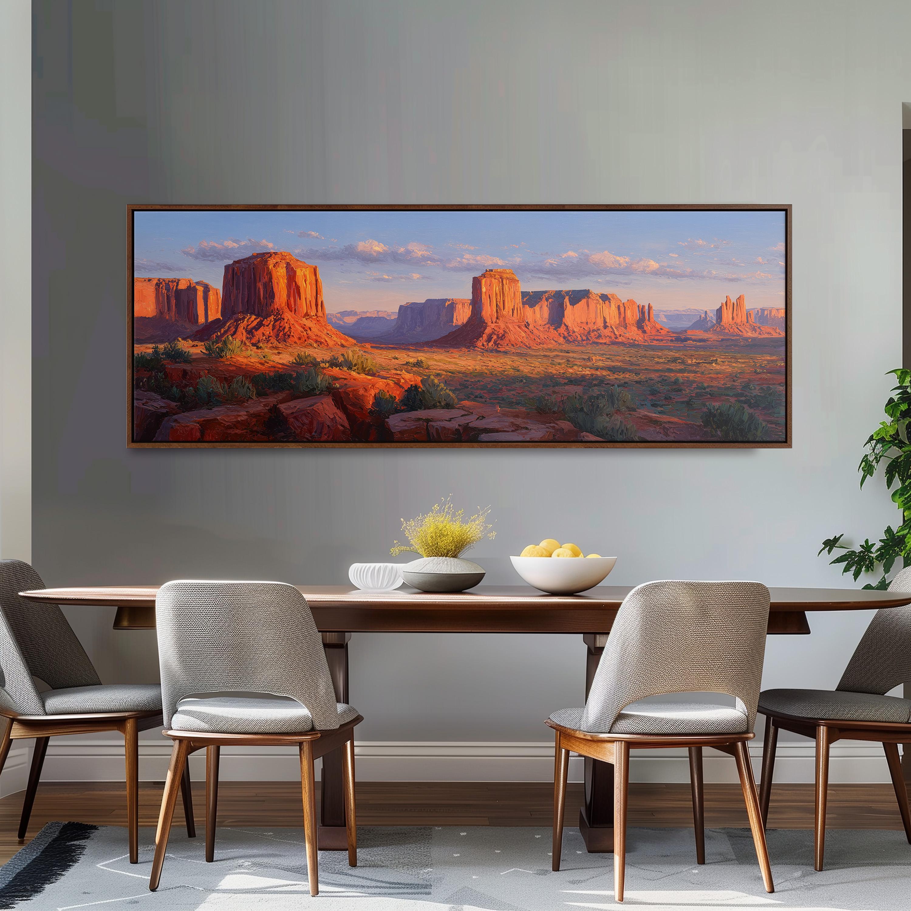 a large framed painting of a desert landscape with mountains in the background, hanging on a wall above a wooden dining table with four chairs.