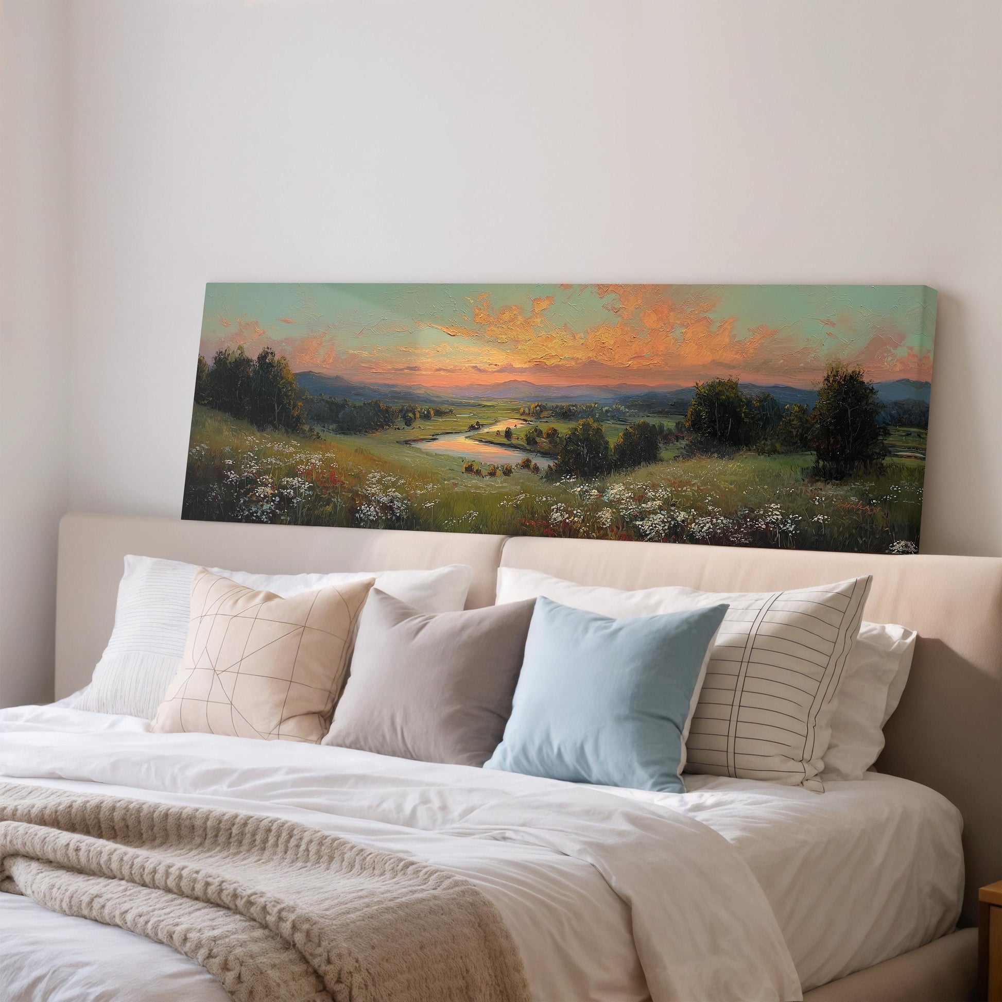 a large landscape painting hanging on a wall above a bed with white pillows and a gray blanket.