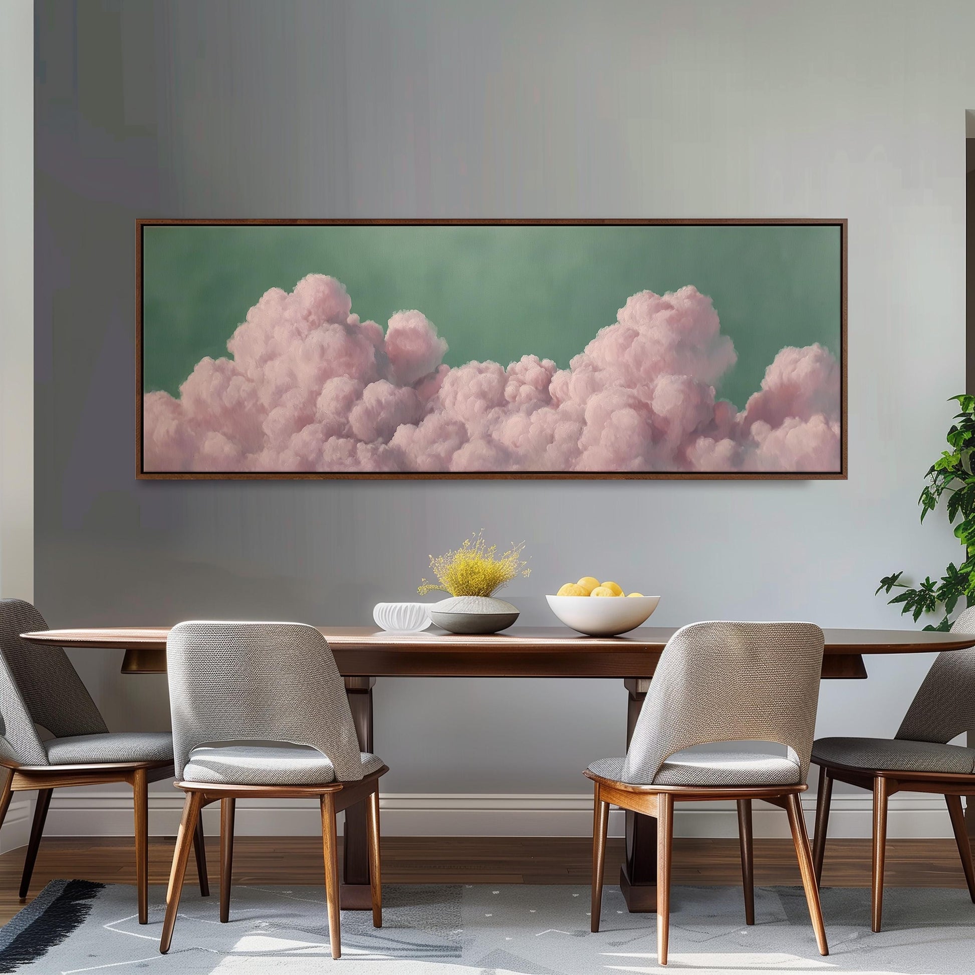 a dining room with a large framed picture of pink clouds hanging on the wall above a wooden dining table with four chairs. The table is set with a bowl of fruit and a vase of flowers, creating a cozy and inviting atmosphere.