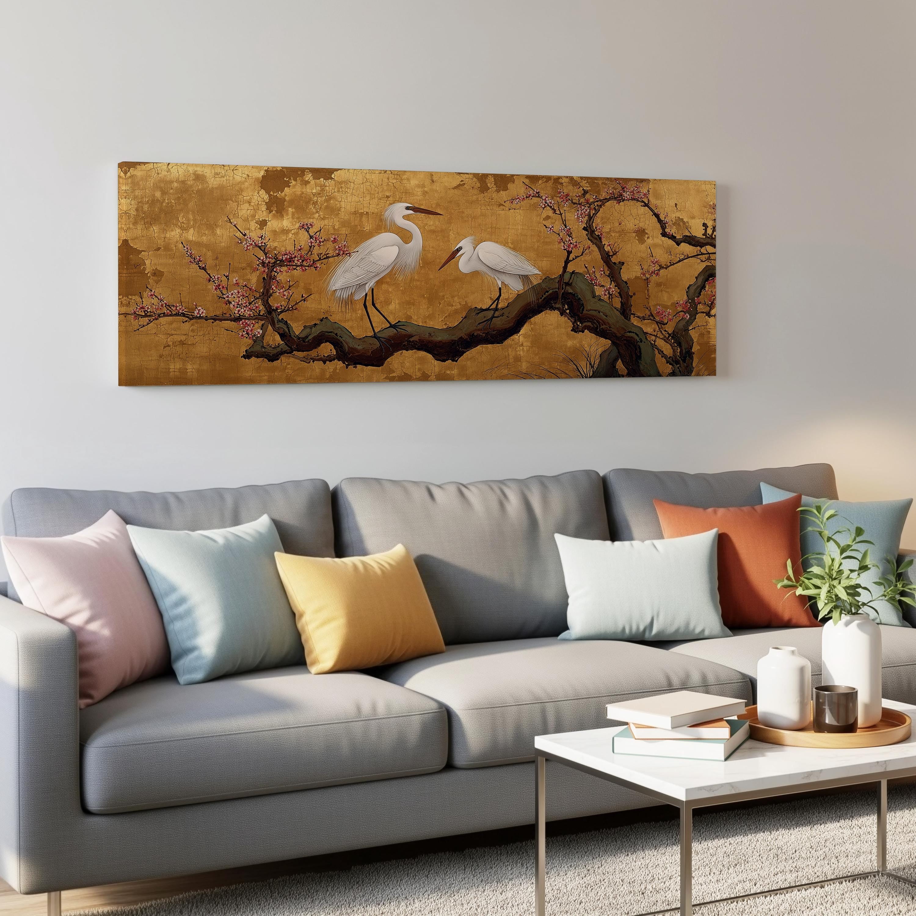 a gray couch with colorful throw pillows, a coffee table, and a large wall art depicting two white birds perched on a branch with pink flowers.