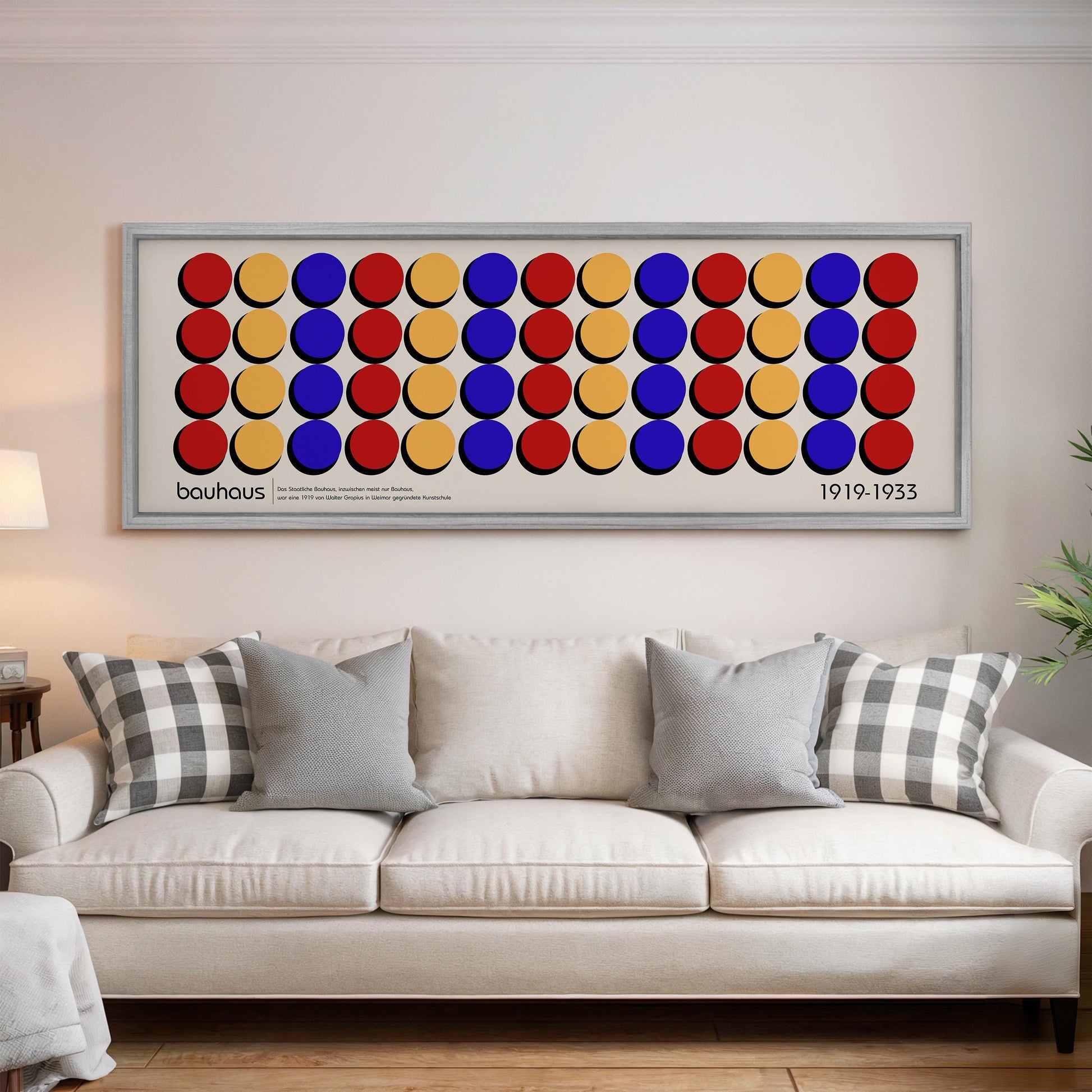 a large framed poster of a colorful geometric design with circles on a white wall above a white couch with patterned pillows.