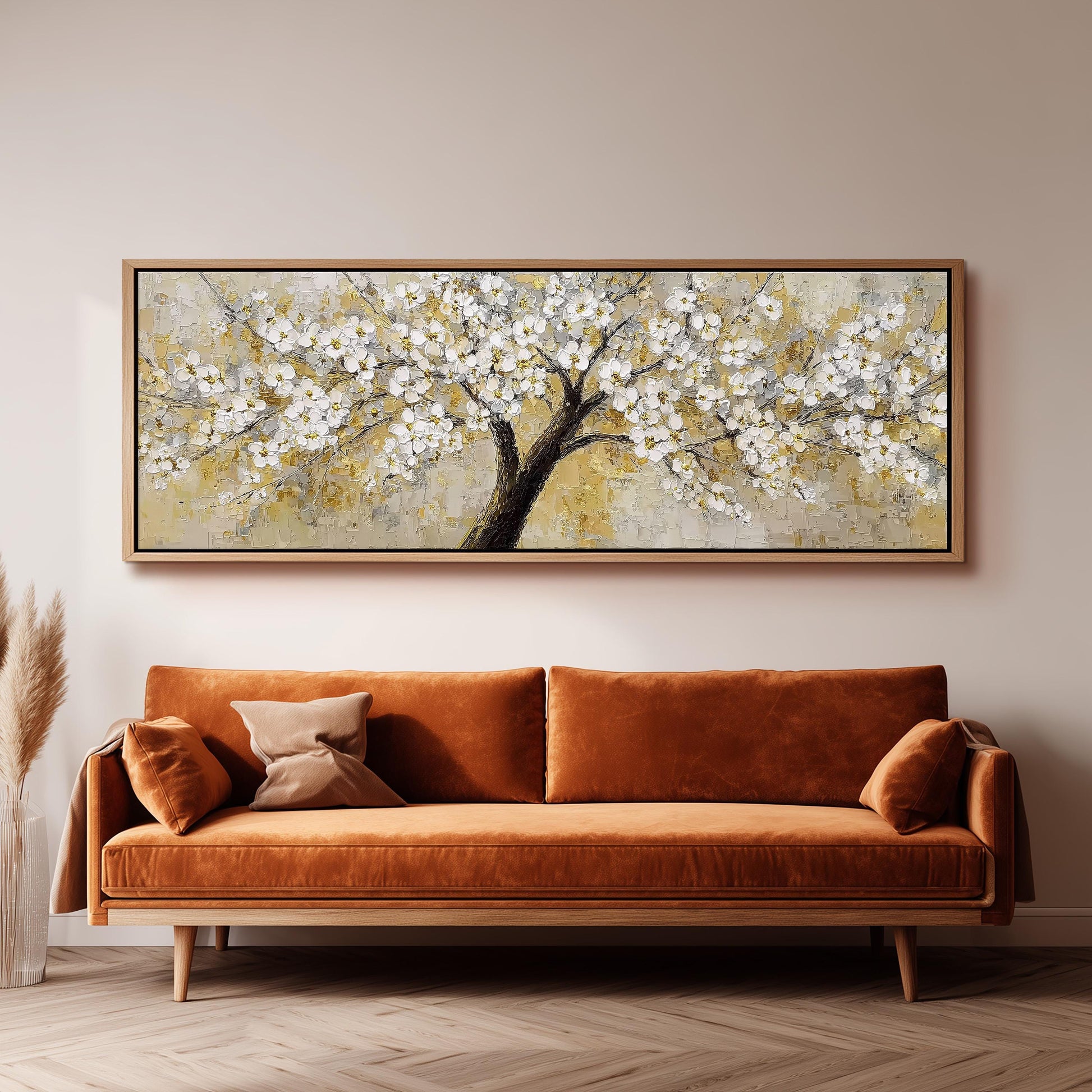 a large painting of a tree with white flowers hanging on the wall above a brown sofa.