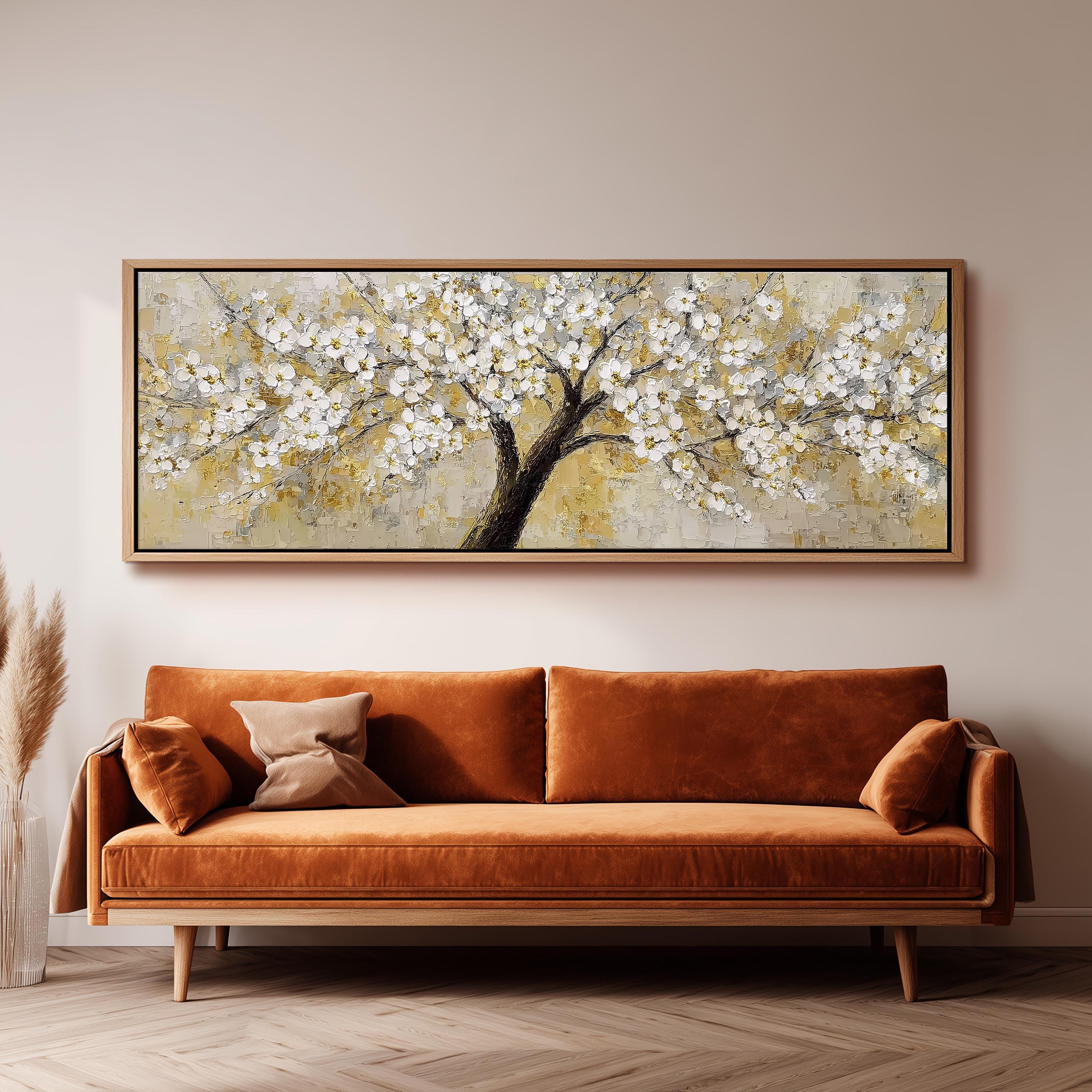 a large painting of a tree with white flowers hanging on the wall above a brown sofa.