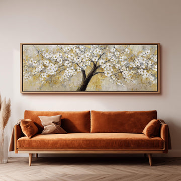 a large painting of a tree with white flowers hanging on the wall above a brown sofa.