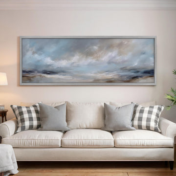 a large, framed painting of a cloudy sky hanging above a white sofa with gray and white plaid throw pillows.