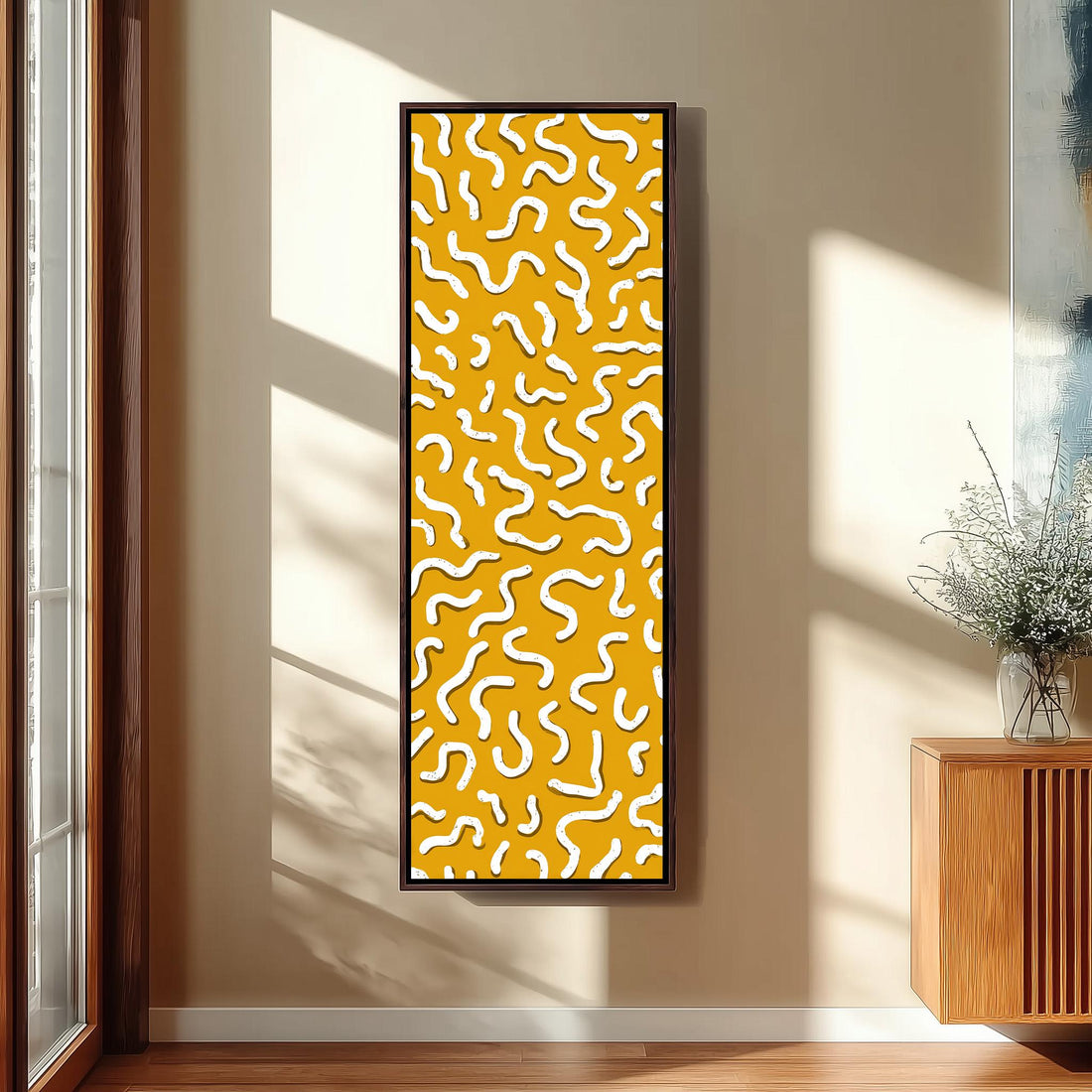 a large, abstract painting with a yellow and white color scheme, hanging on a wall in a room with a wooden cabinet and a vase of flowers.