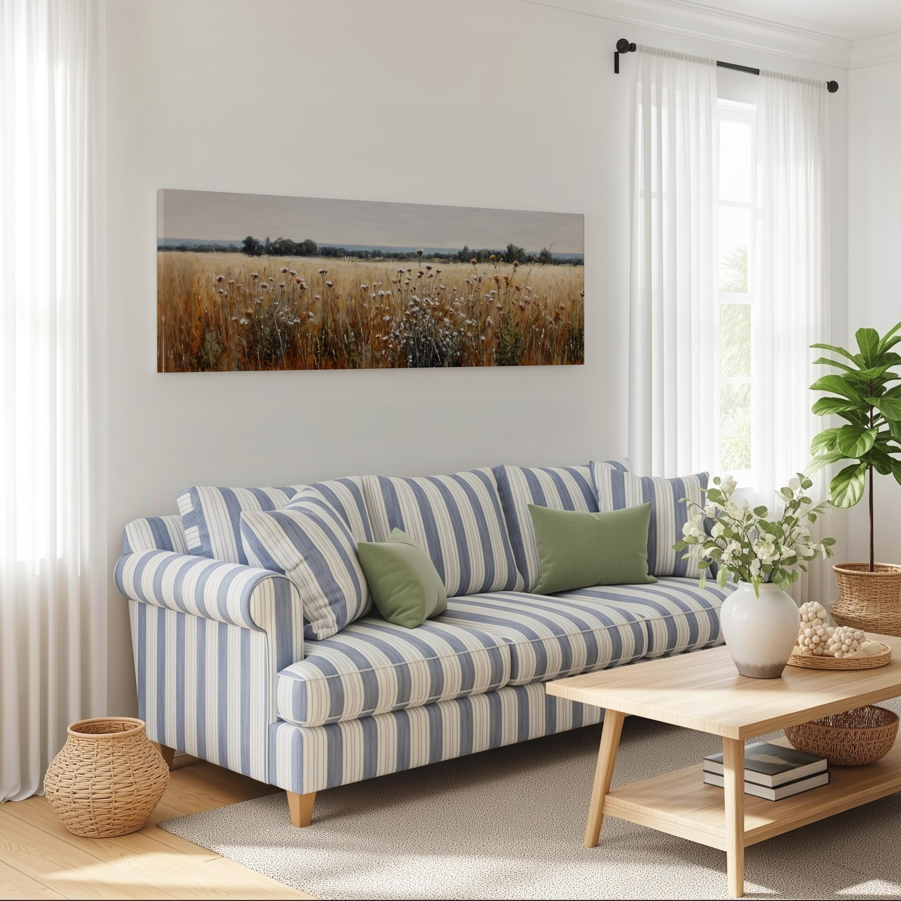 a cozy living room with a striped blue and white sofa, a wooden coffee table, and a large window with white curtains. Above the sofa, there is a large canvas print of a field with wildflowers. The room also features a potted plant, a basket, and some books, creating a warm and inviting atmosphere.