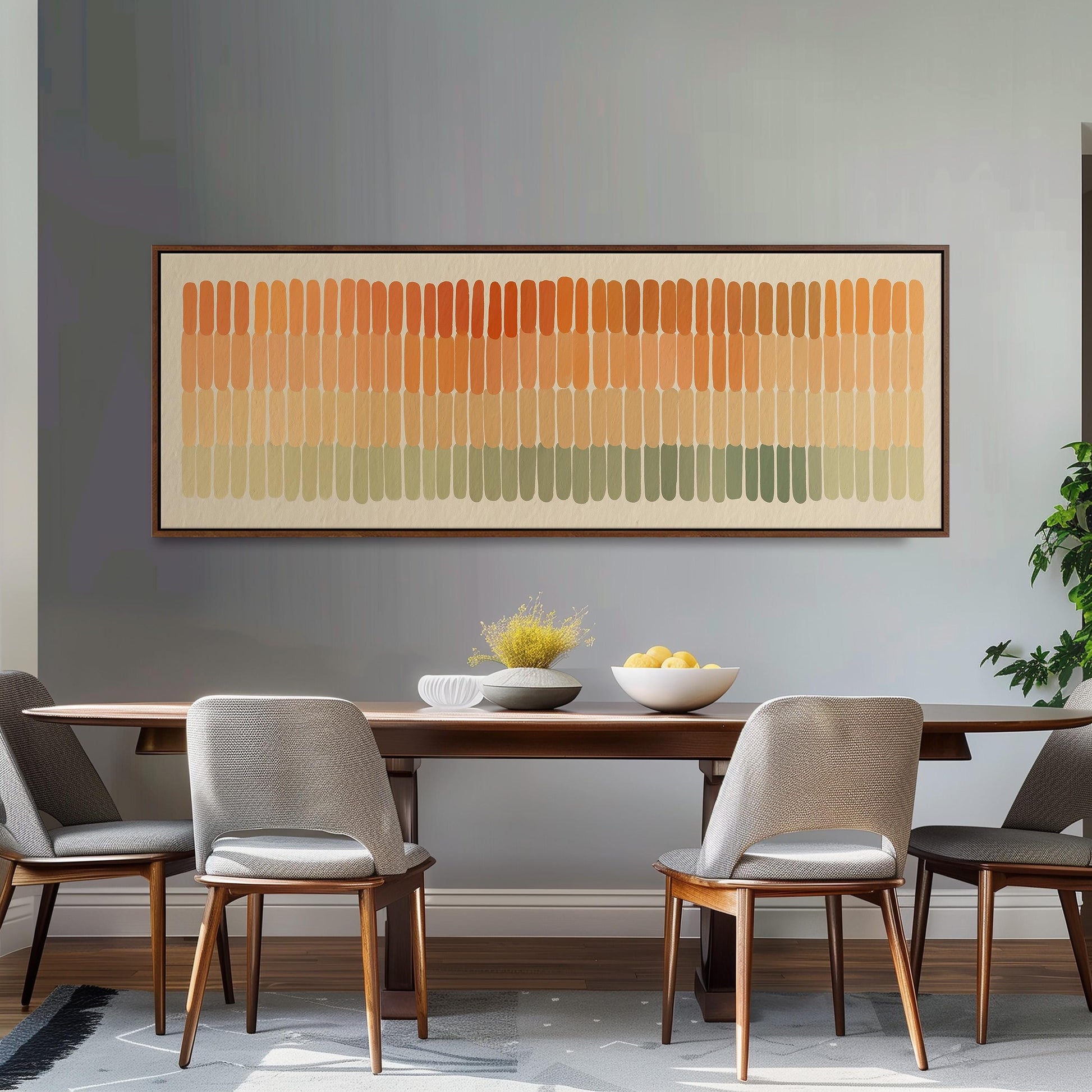 a dining room with a wooden table and four gray chairs. Above the table, there is a large abstract painting with horizontal stripes in various shades of orange, yellow, and green. The table is set with a bowl of fruit and a vase of flowers, creating a warm and inviting atmosphere.