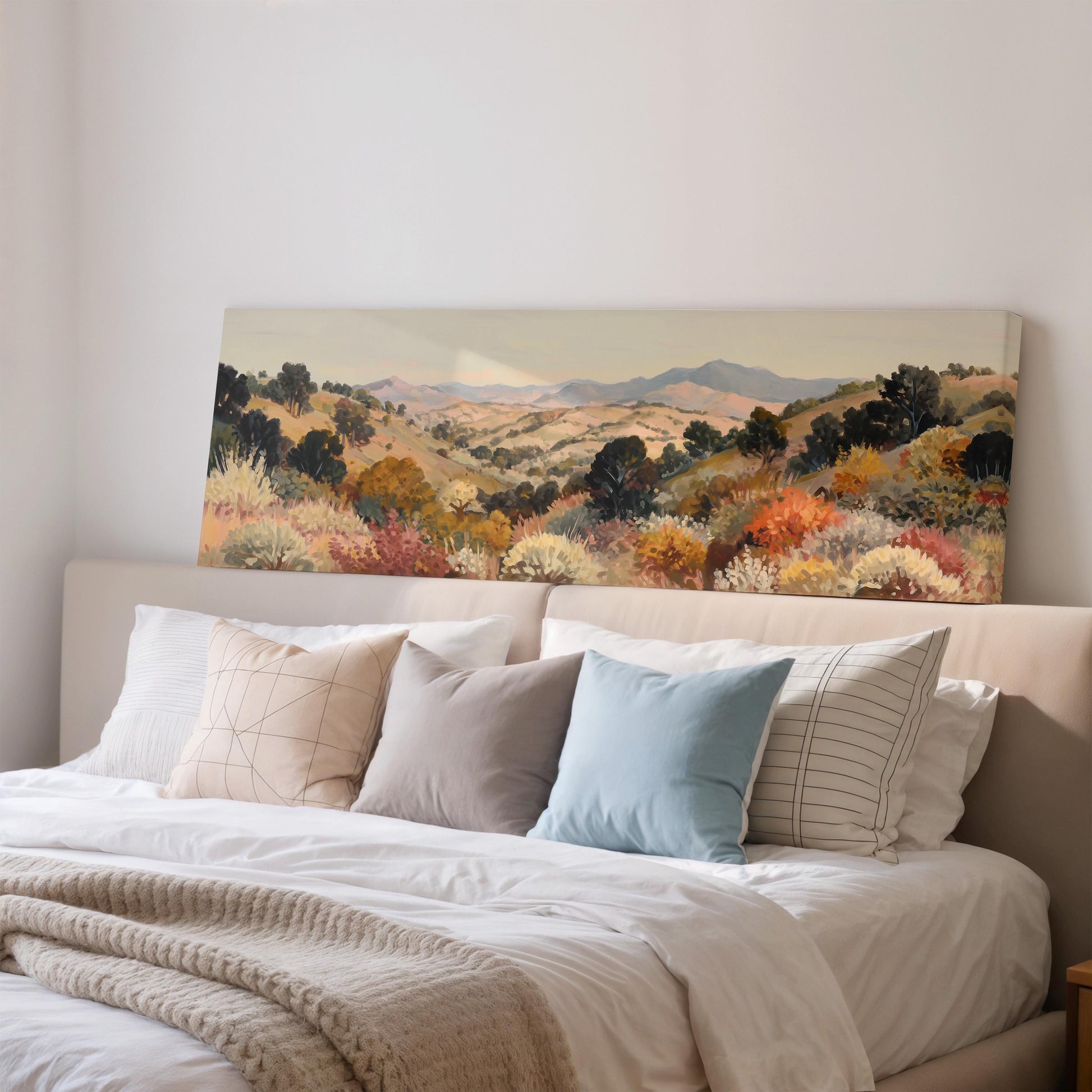 a large landscape painting hanging on a wall above a bed with white pillows and a gray blanket.