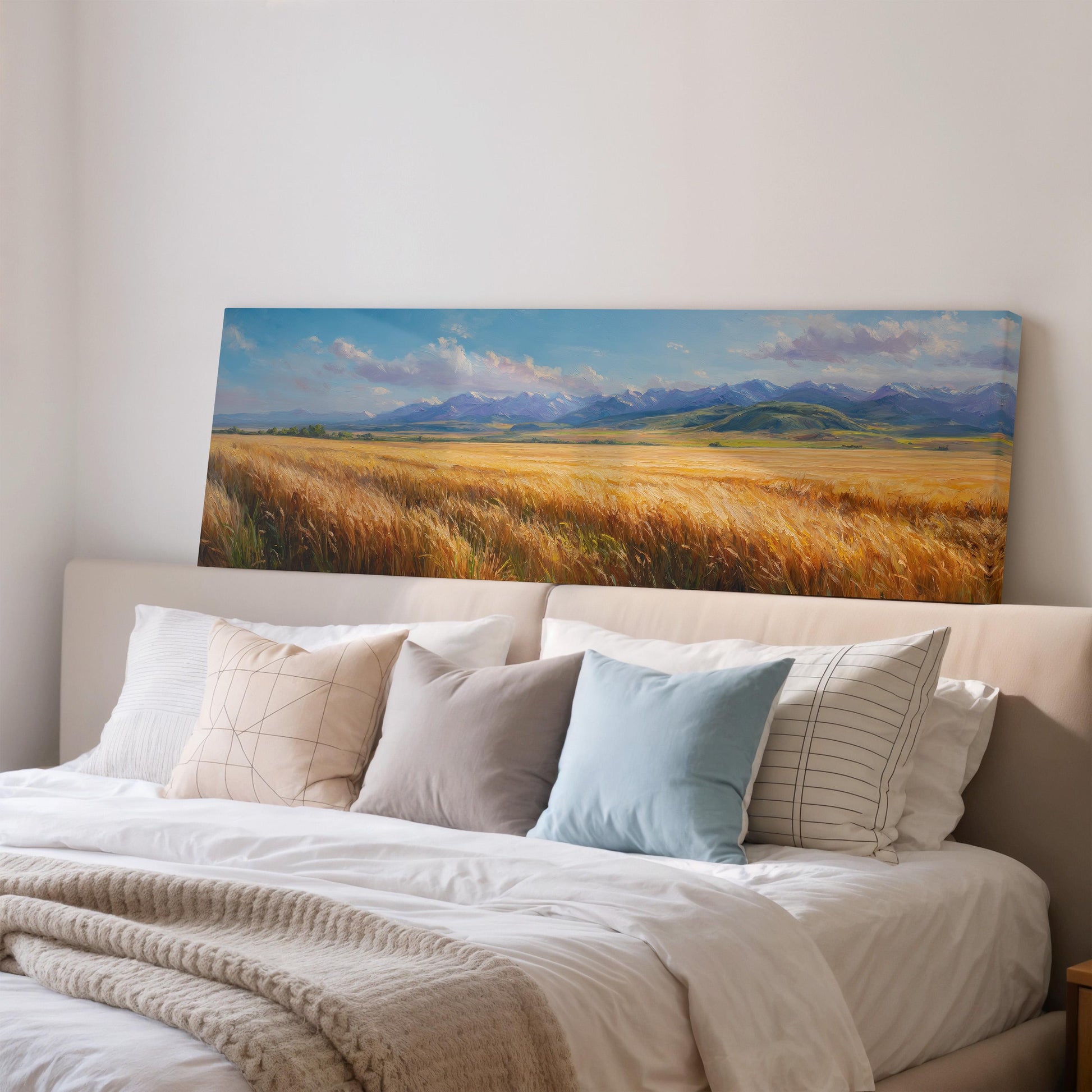 a large painting of a field of golden wheat hanging on a wall above a bed with white pillows and a gray blanket.