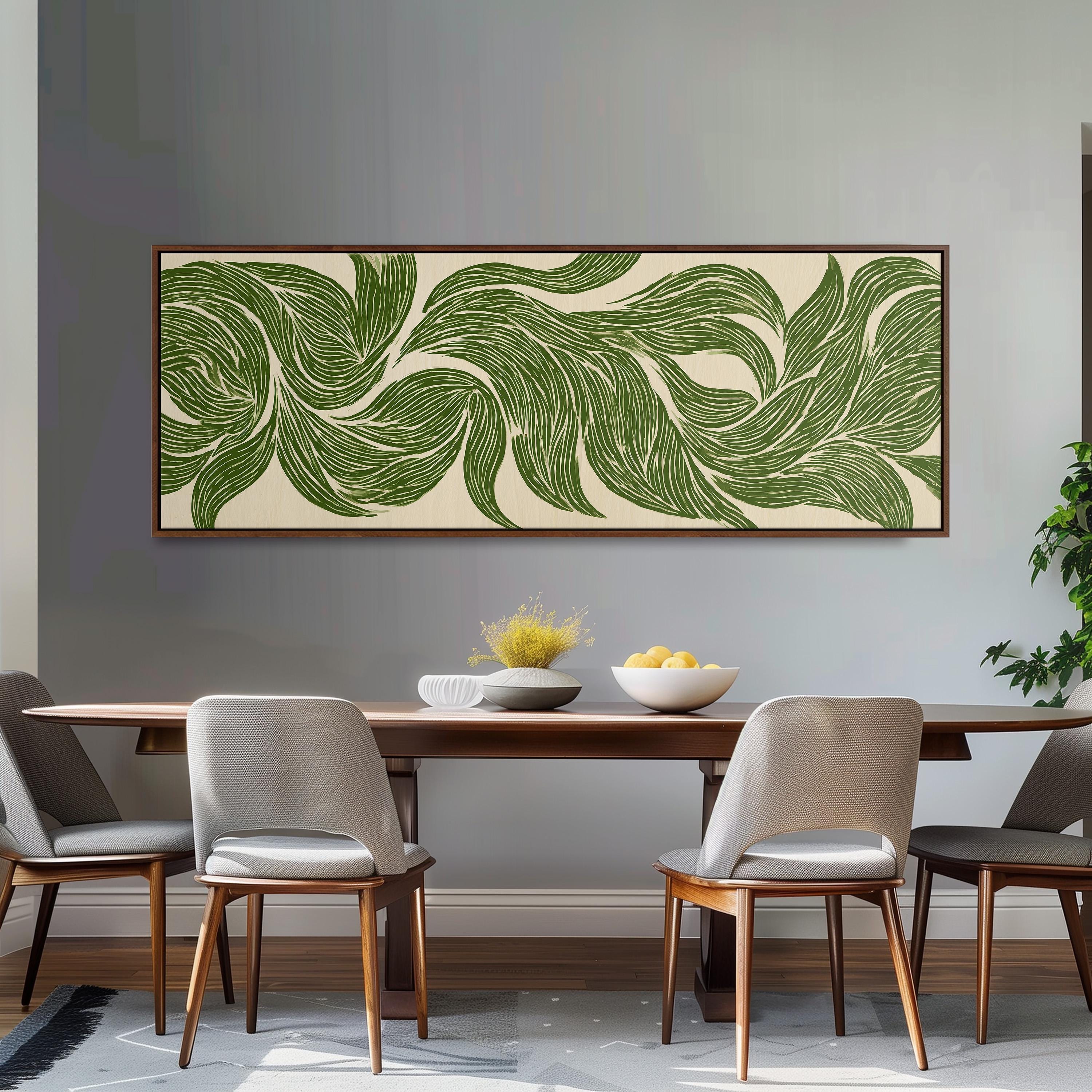 a dining room with a wooden table and four chairs. Above the table, there is a large framed artwork depicting green leaves and flowers. The table is set with a bowl of fruit and a vase of flowers, creating a cozy and inviting atmosphere.
