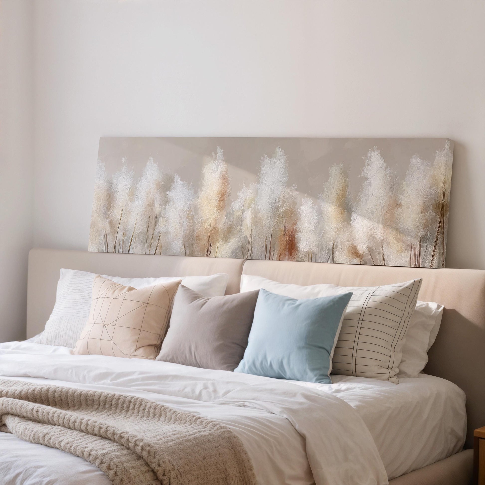 a well-made bed with a neutral color scheme, featuring a large pillow and a smaller pillow. Above the bed, there is a painting of tall grasses in a field, which adds a natural element to the room's decor.