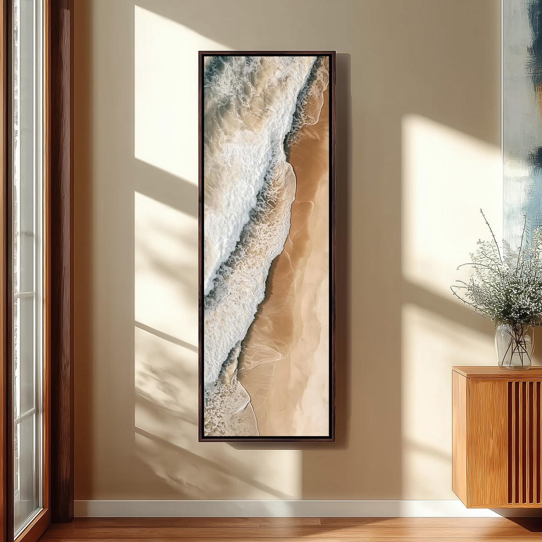 a large framed painting of a beach scene hanging on a wall, with a wooden chair and a small table in the foreground.