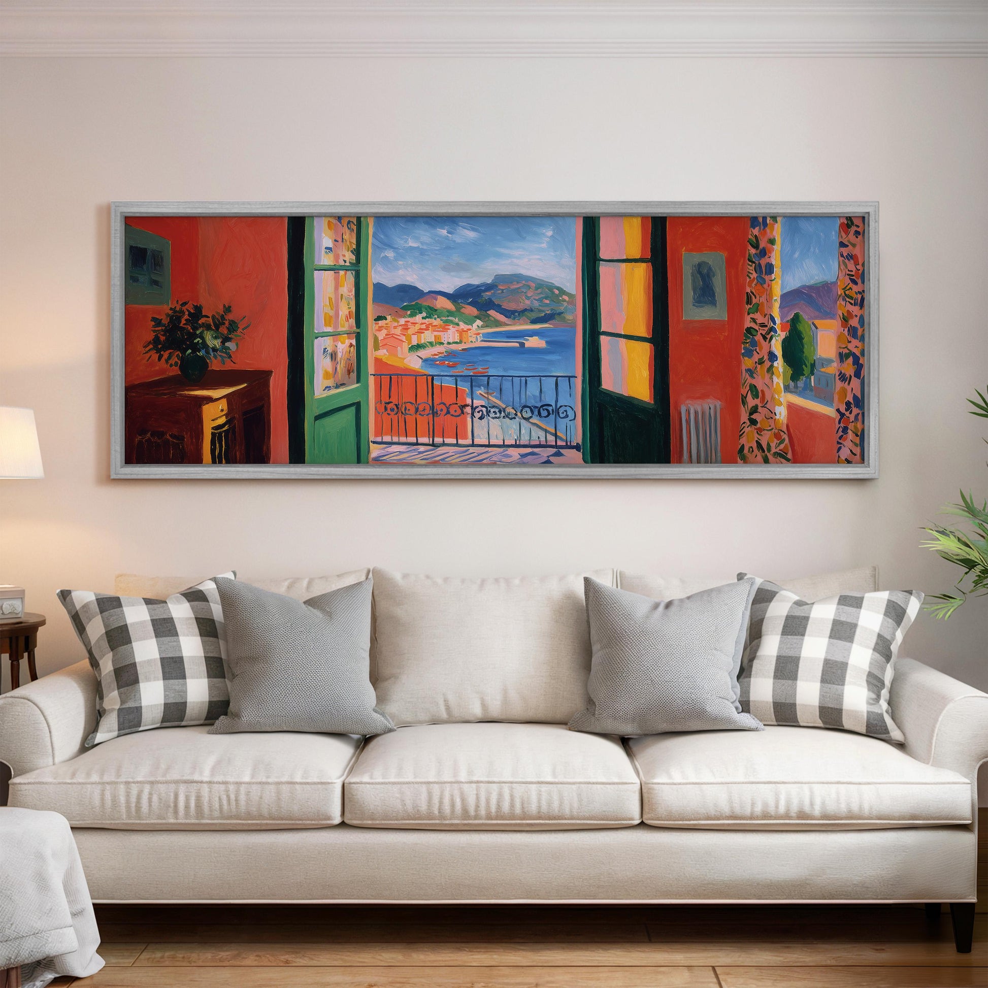 a large, colorful painting of a balcony overlooking a scenic view, hanging on a wall above a white couch with patterned throw pillows.