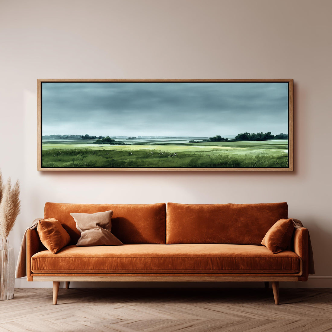 a large landscape painting hanging on a wall above a brown sofa with orange cushions.