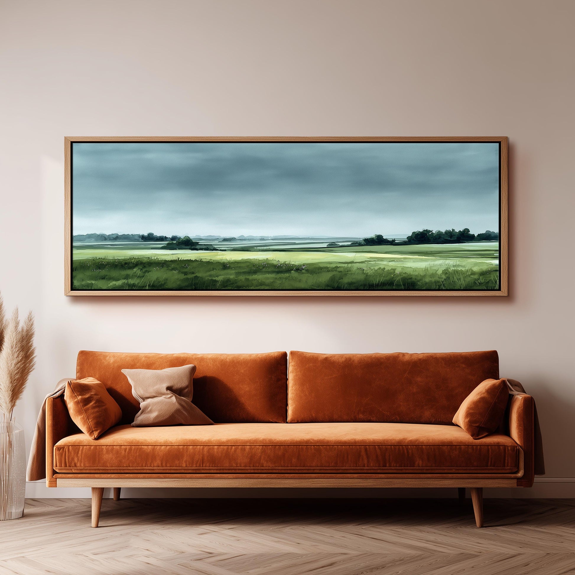a large landscape painting hanging on a wall above a brown sofa with orange cushions.