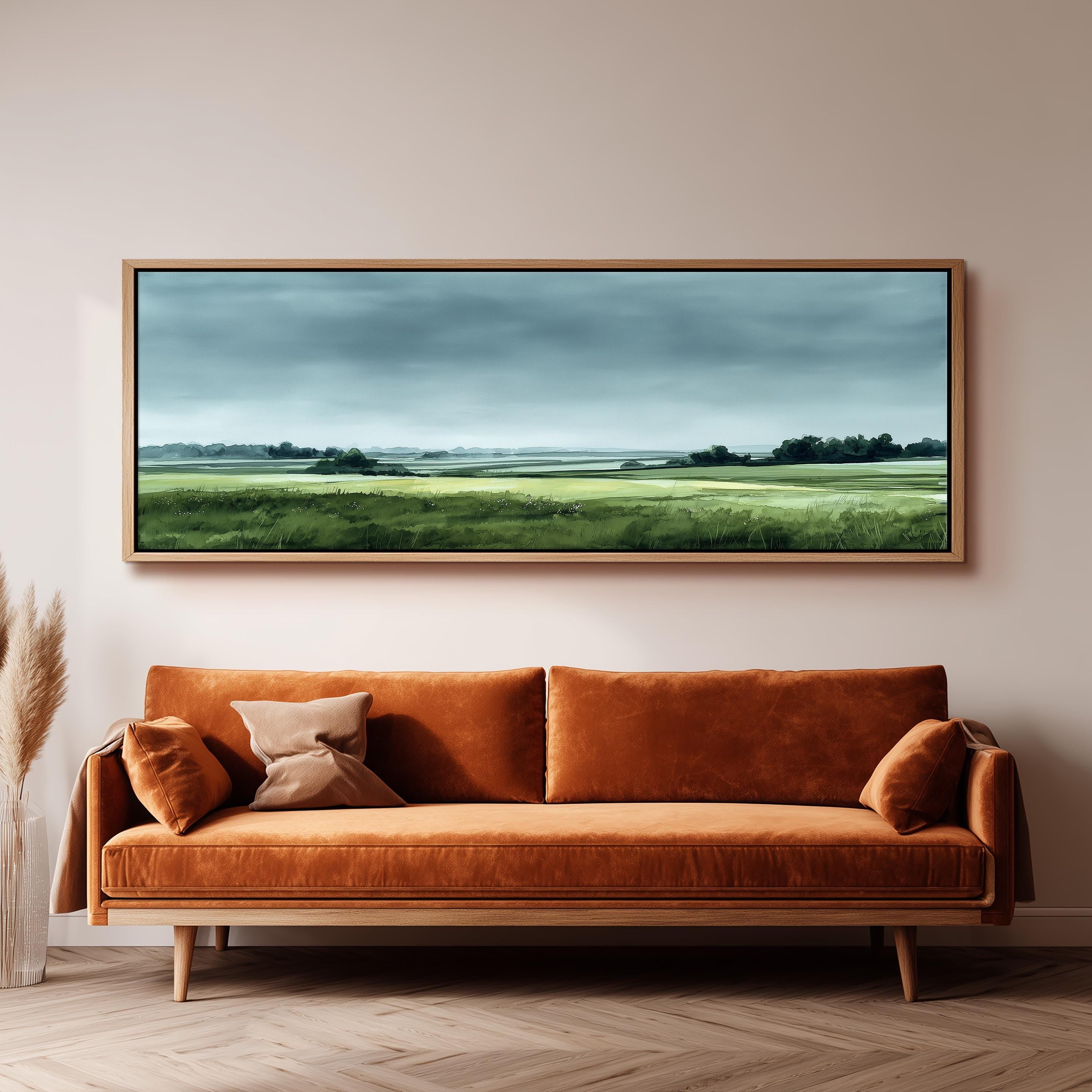 a large landscape painting hanging on a wall above a brown sofa with orange cushions.