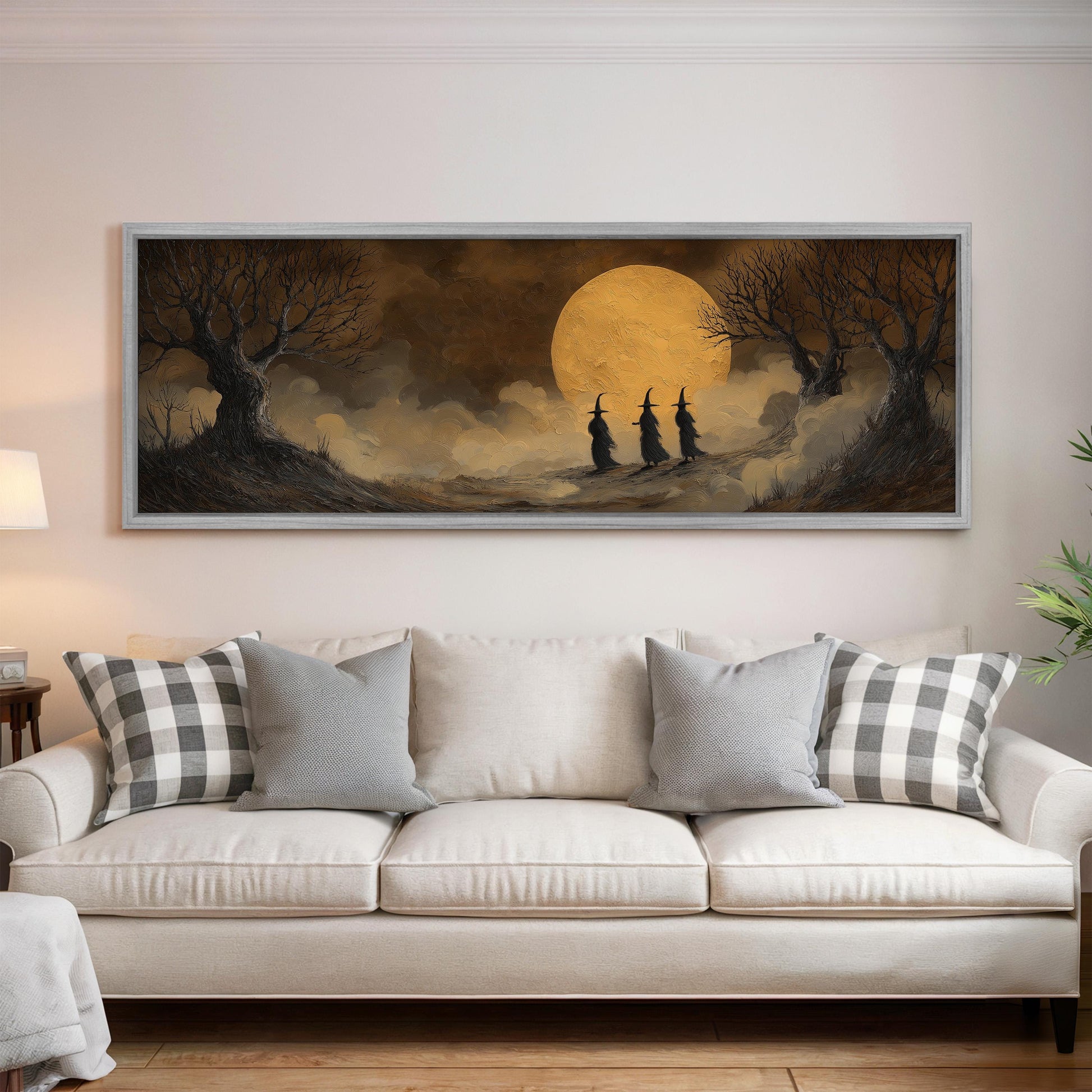 a large painting of three witches walking under a large moon on a dark background, hanging on a wall above a white couch with plaid throw pillows.