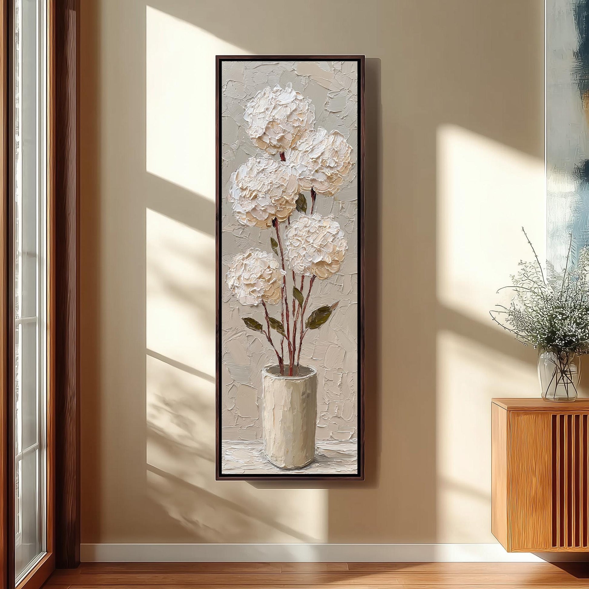 a large painting of white hydrangeas in a vase, hanging on a wall in a room with a wooden cabinet and a window.