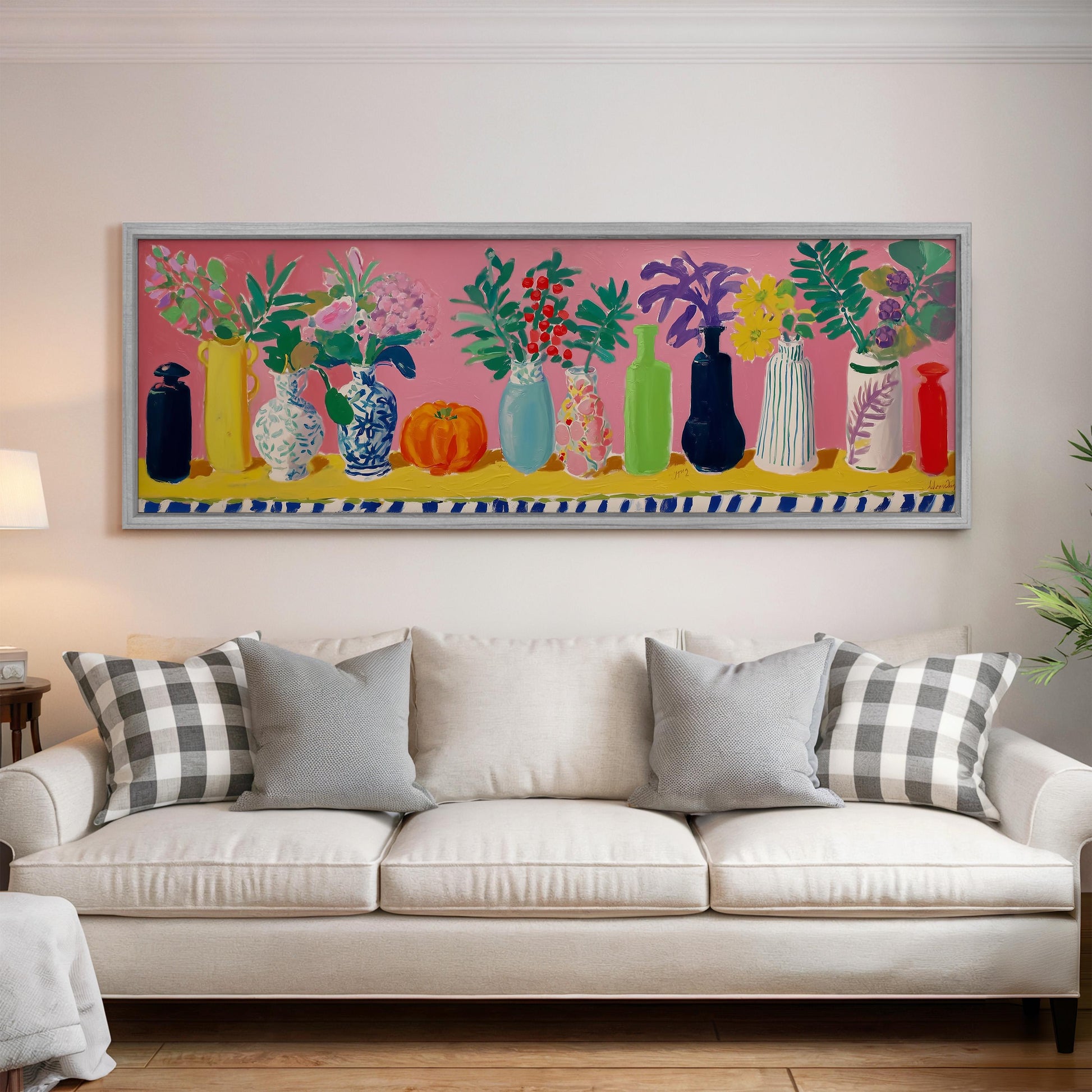 a large, colorful painting of various vases and flowers displayed on a wall above a white couch with plaid pillows.
