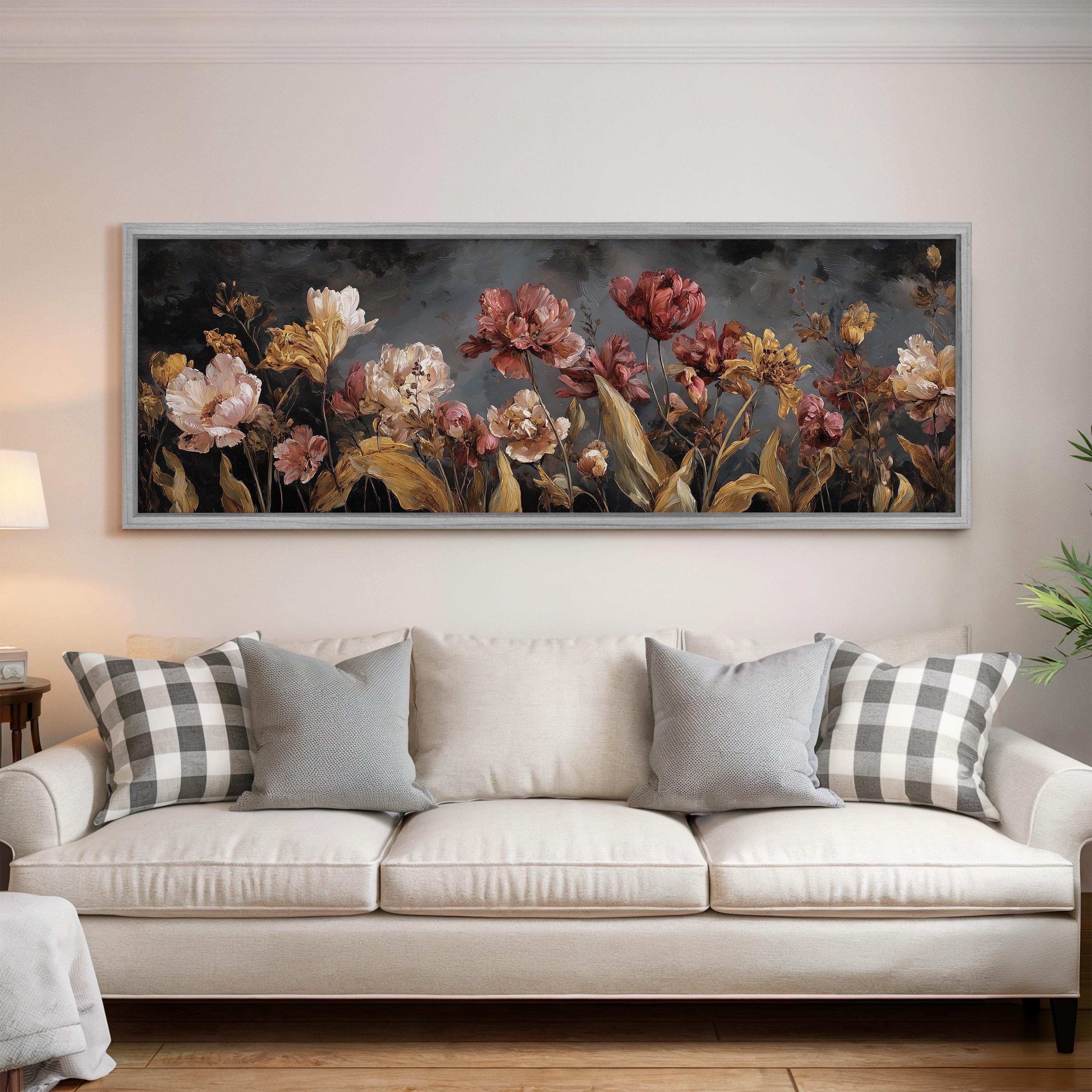 a large, framed painting of flowers hanging on a wall above a white couch with gray and white plaid throw pillows.