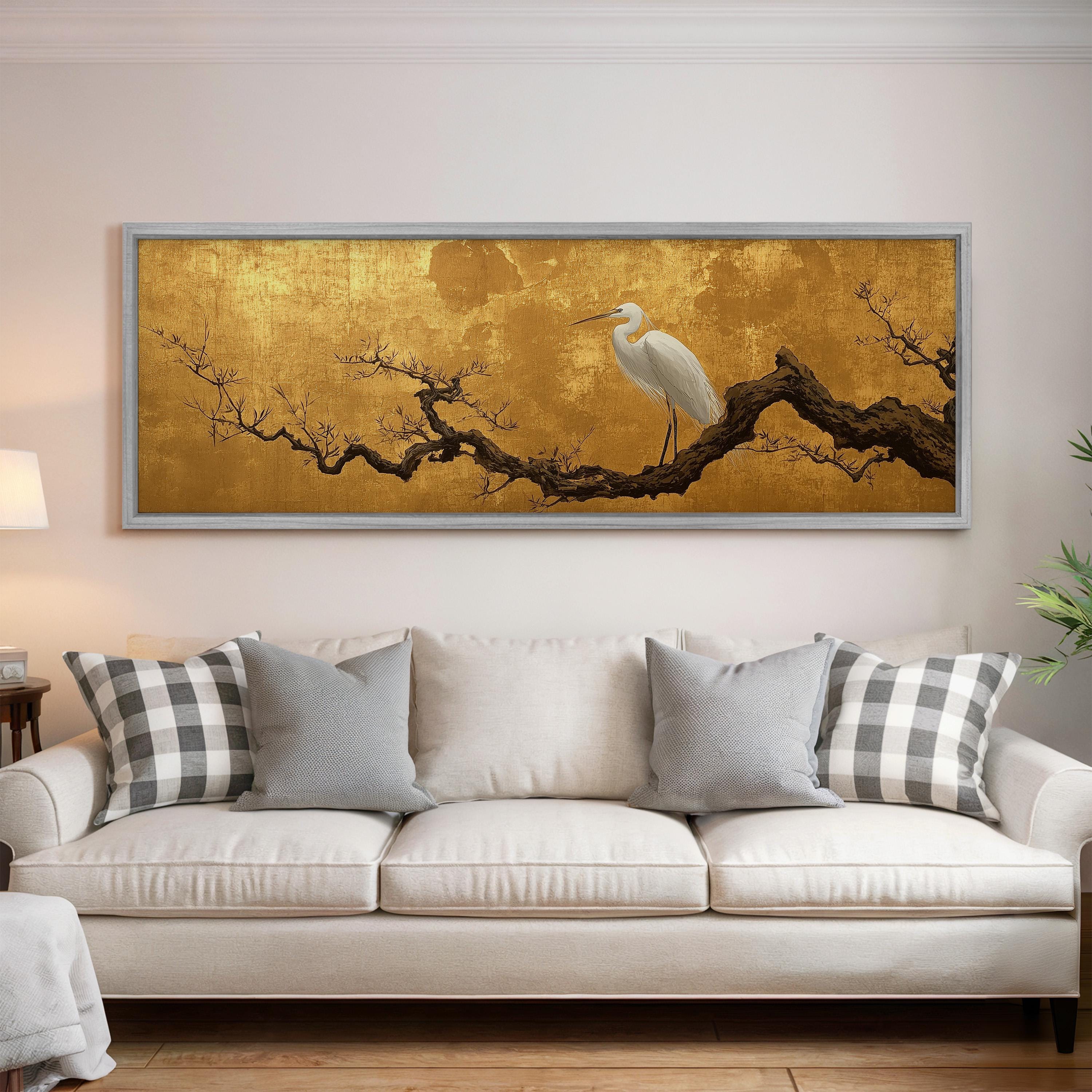a large, framed painting of a white heron perched on a branch, hanging on a wall above a white couch with gray and white plaid throw pillows.