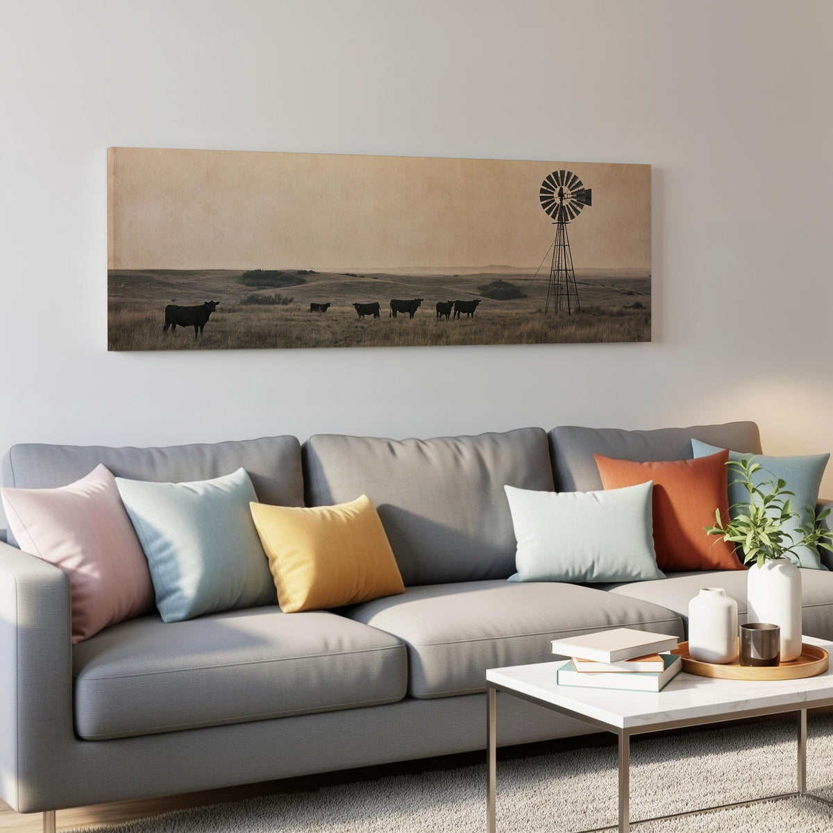 Black cattle grazing by a windmill on the prairie panoramic canvas print above a grey sofa in a living room