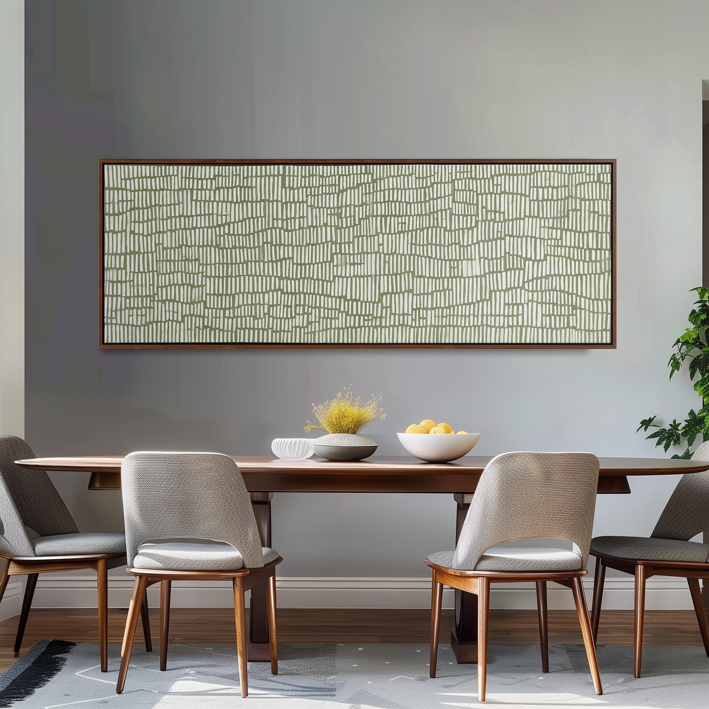 a modern dining room with a wooden table and four gray chairs. Above the table, there is a large abstract painting with a geometric pattern in shades of green and white. On the table, there is a bowl of fruit and a vase of flowers, adding a touch of color and life to the space.