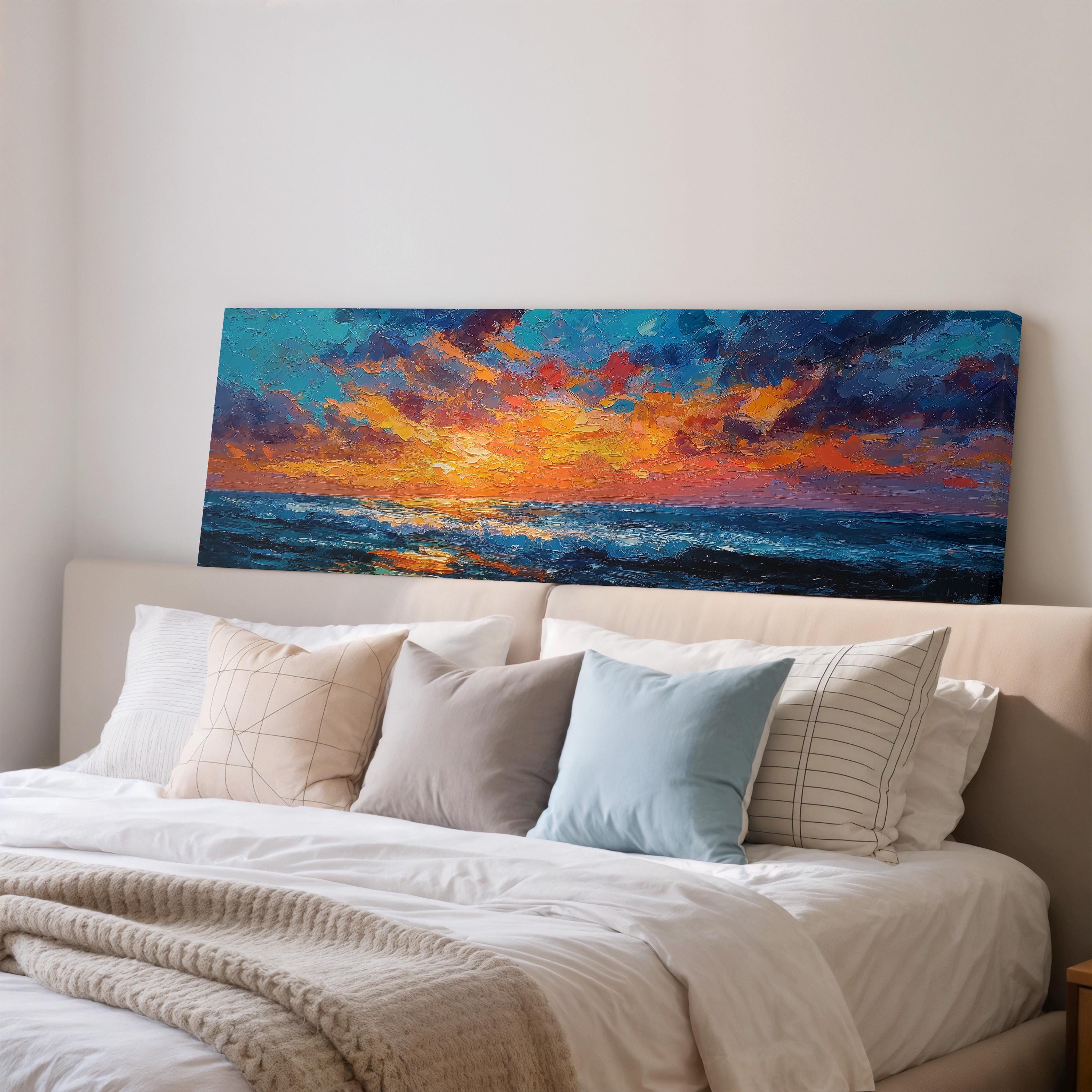 a large painting of a sunset over the ocean, hanging on a wall above a bed with white pillows and a gray blanket.